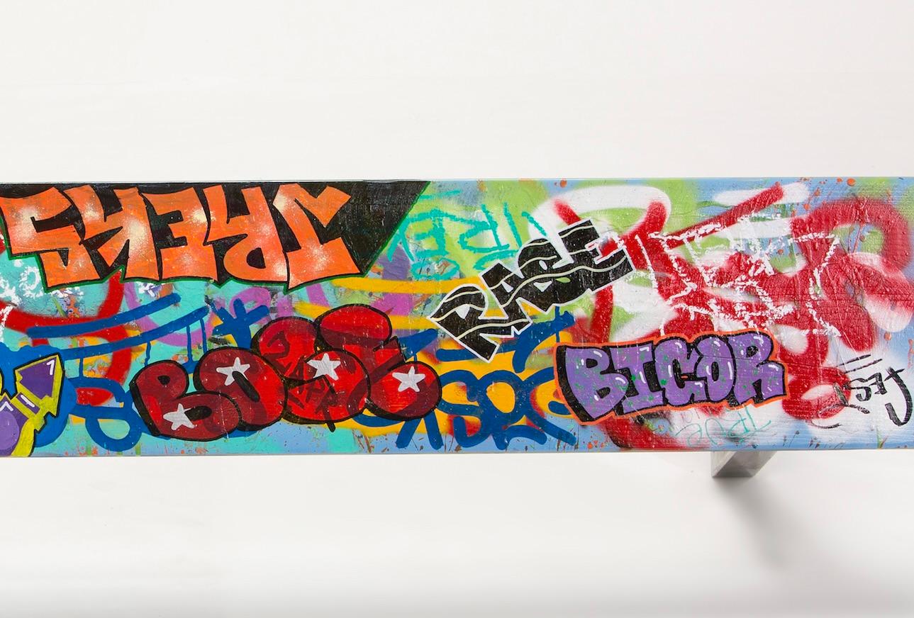 Fun, unique, one-of-a-kind tagged graffiti wood bench, with colorful graffiti tags covering the top and underside of the wood seat.   

Material: Spray paint, paint pens, and polyurethane on wood with steel legs   
Size: 68 x 11 x 16.5 in (L x W x