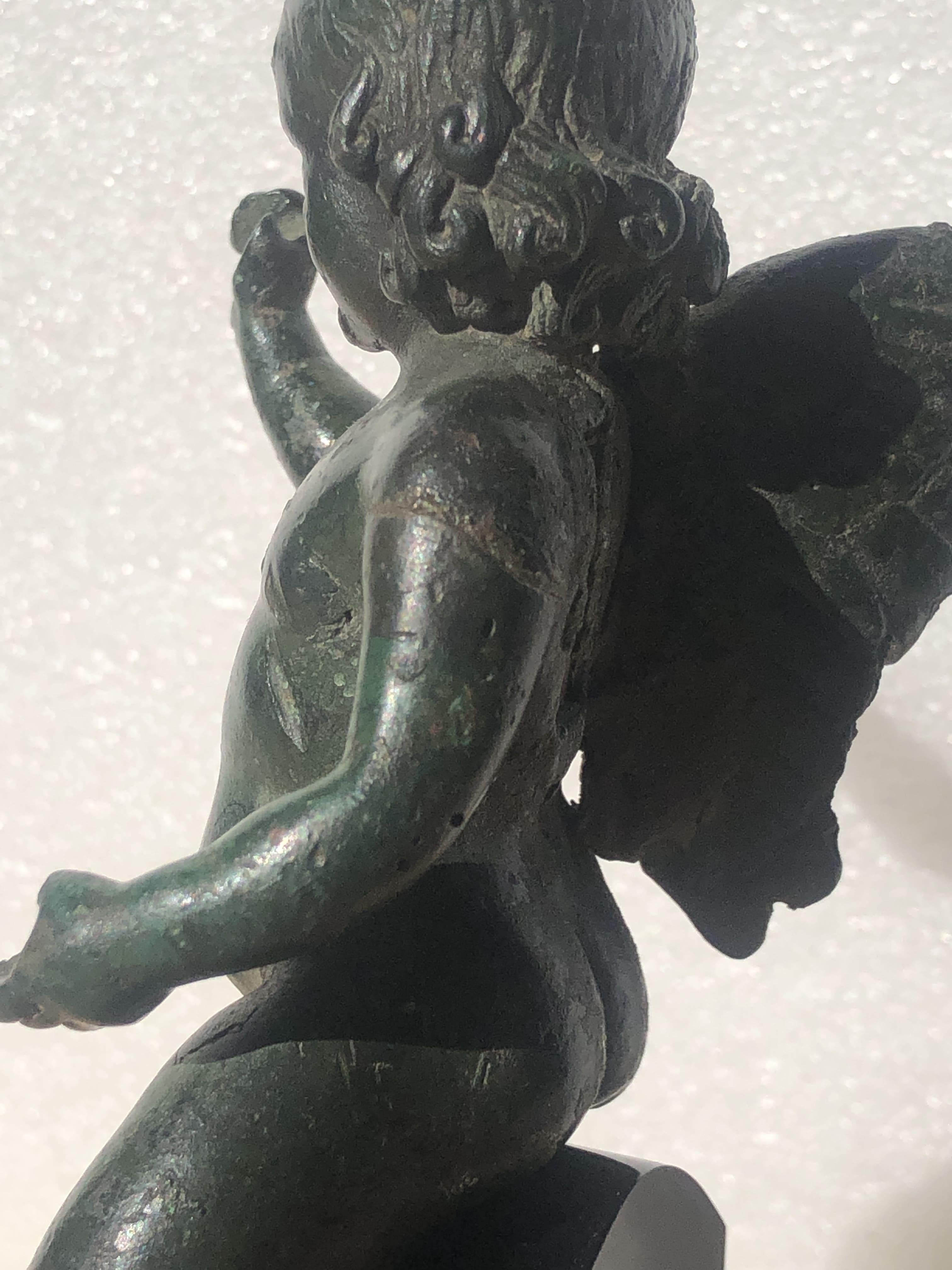 Bronze figure of a young Eros, caught in the pose of riding a dolphin.
Attractive green patina, some fingers and right foot are broken. Separately worked left wing is missing. Right wing partially bent and with some feathers missing. 

For similar