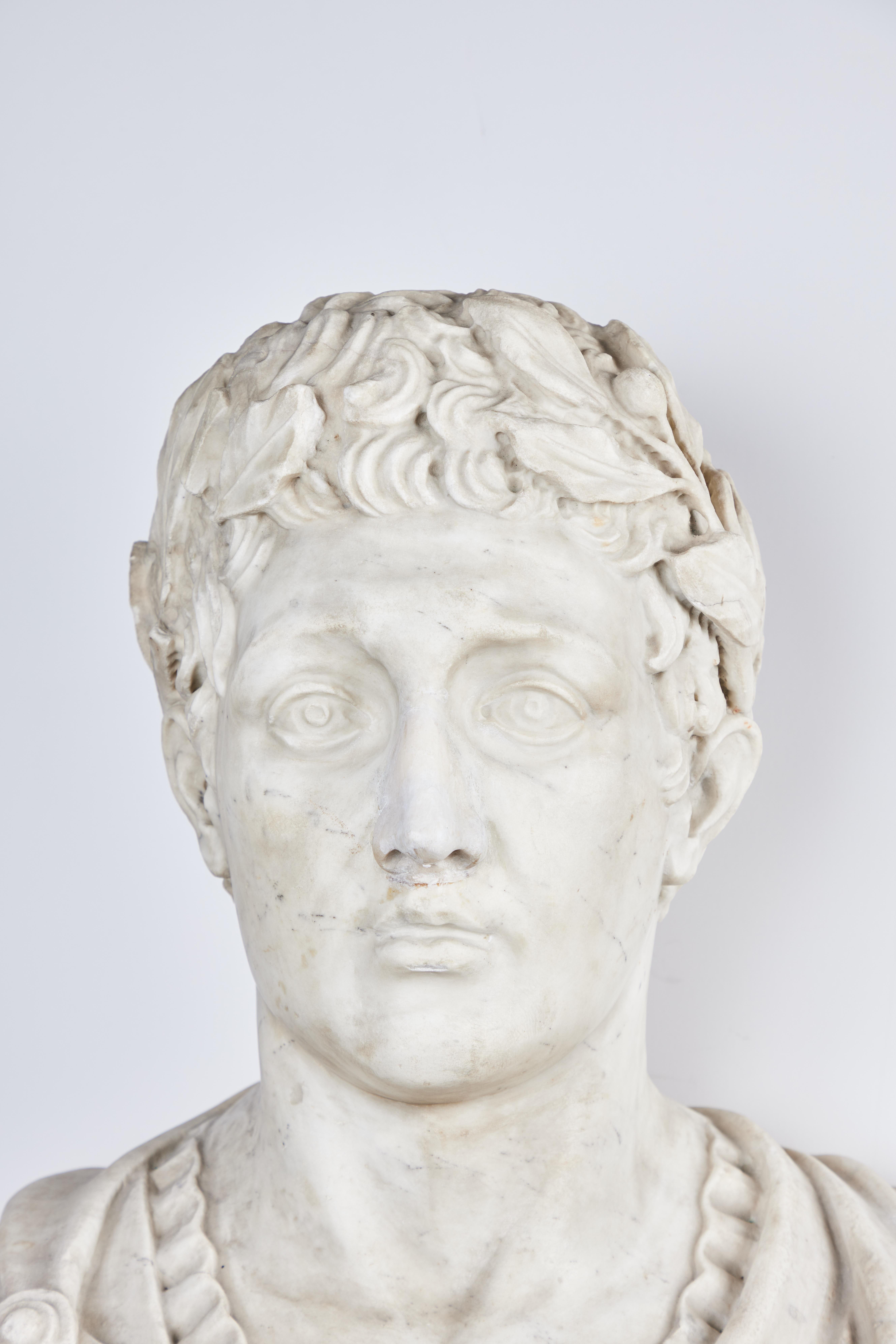 Beautifully hand carved Carrara marble bust of a Roman Emperor on a variegated marble base, elaborately robed with a laurel wreath adorning his head.