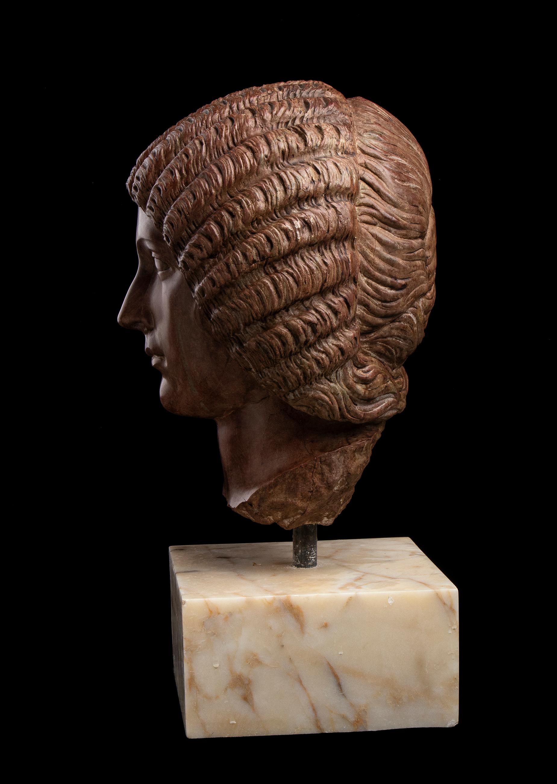 Marble sculpture depicting a detailed portrait of the Roman Empress Julia Domna, sculpted by a master Roman sculptor in red marble and mounted on a square white marble base with a central metal pin.
The sculpture is crafted from rosso antico marble