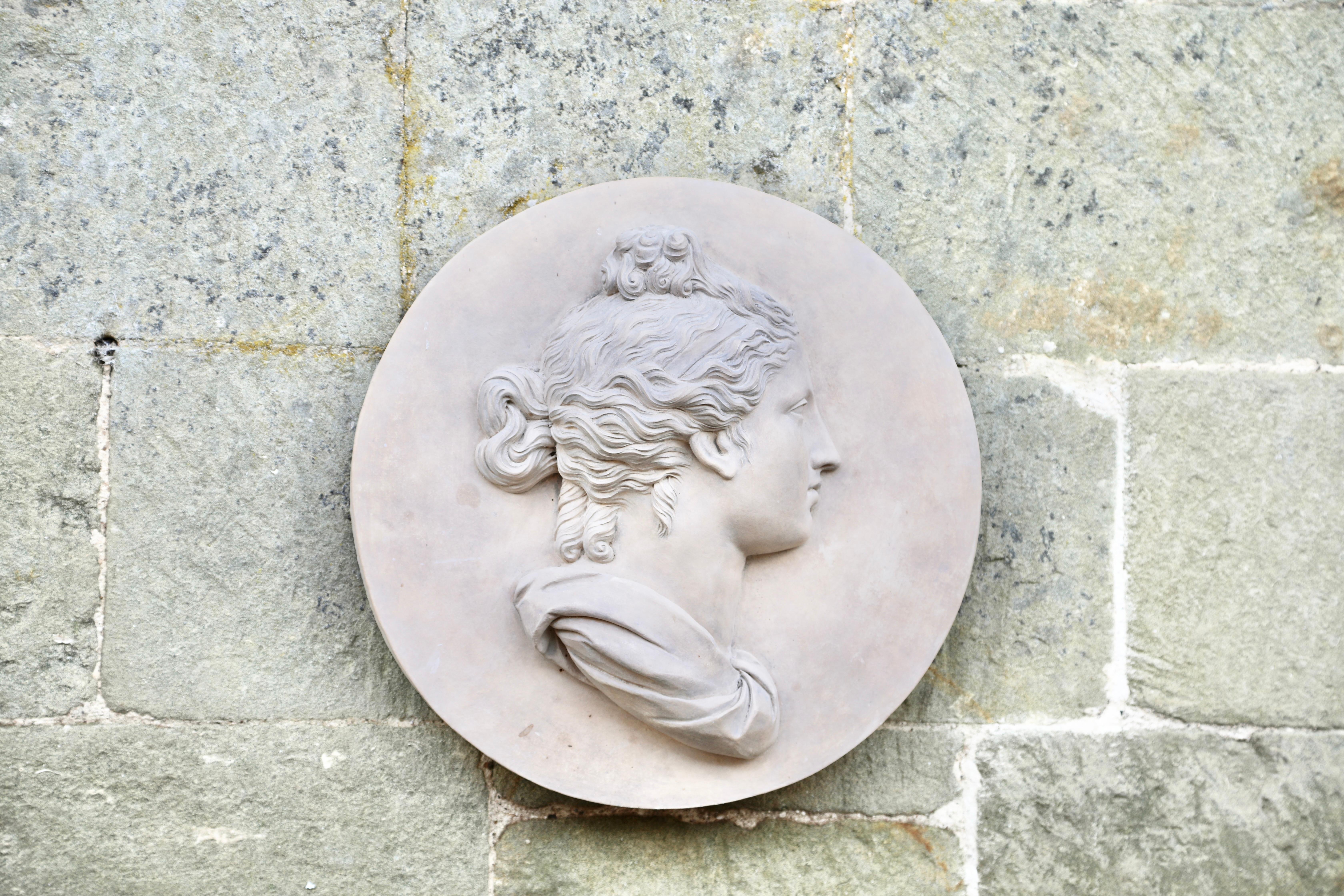 The roundel is crafted from Ceramic Stoneware and is a modern rendition of an 18th-century Coade original, showcasing a neoclassical style. It draws inspiration from classical antique bust models found in Ancient Greece, Rome, and Renaissance