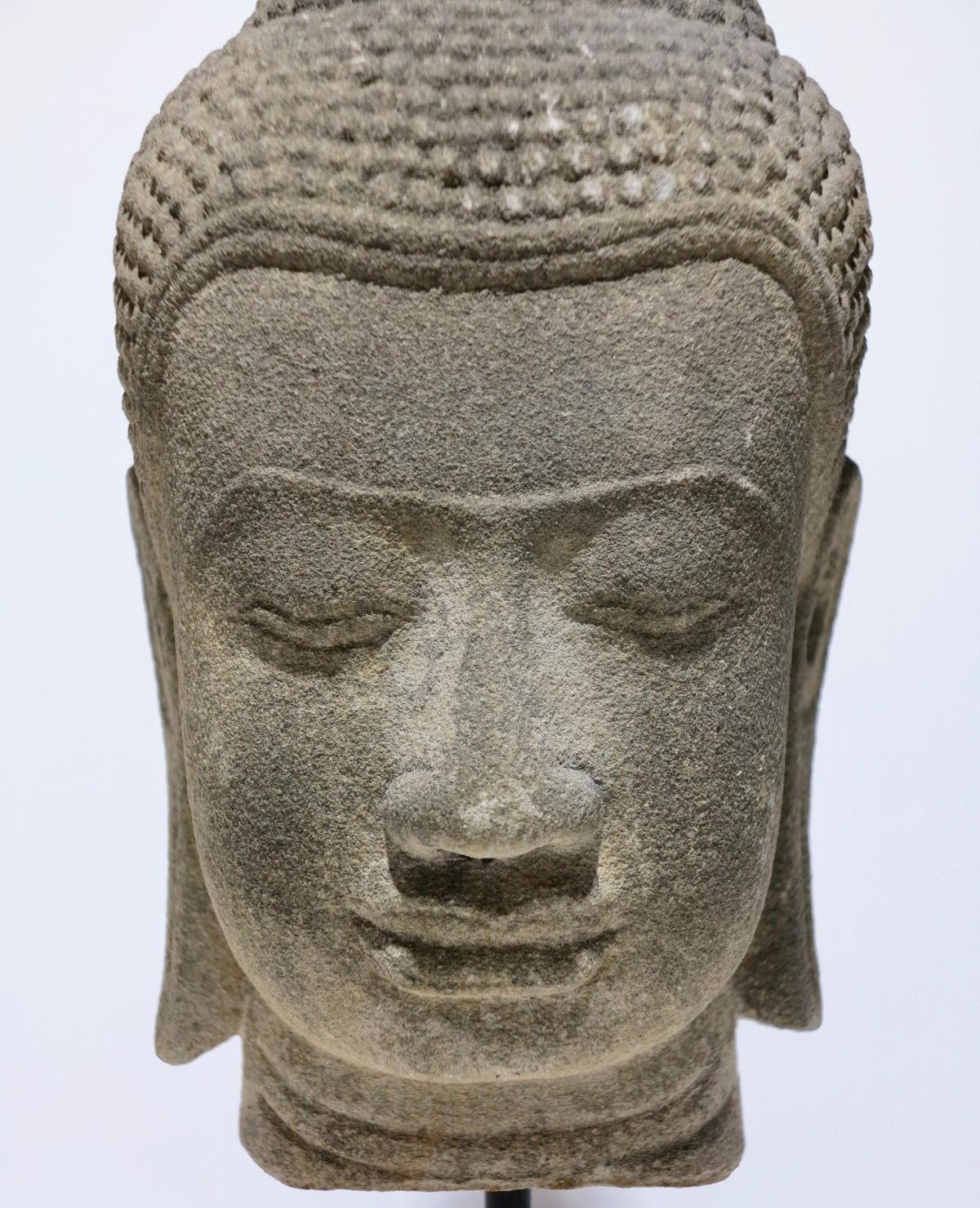 Beautiful Khmer head of Buddha. Angkor period, style of the post-Bayon. 14th century. Carved sandstone. Height 12 5/8 inches, width 5 5/8 inches, profile 5 7/8 inches. Measures 15 5/8 inches tall with stand. No conservation. 