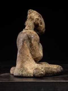 Figure féminine assise, agenouillée sur ses talons, les bras croisés sur la poitrine.