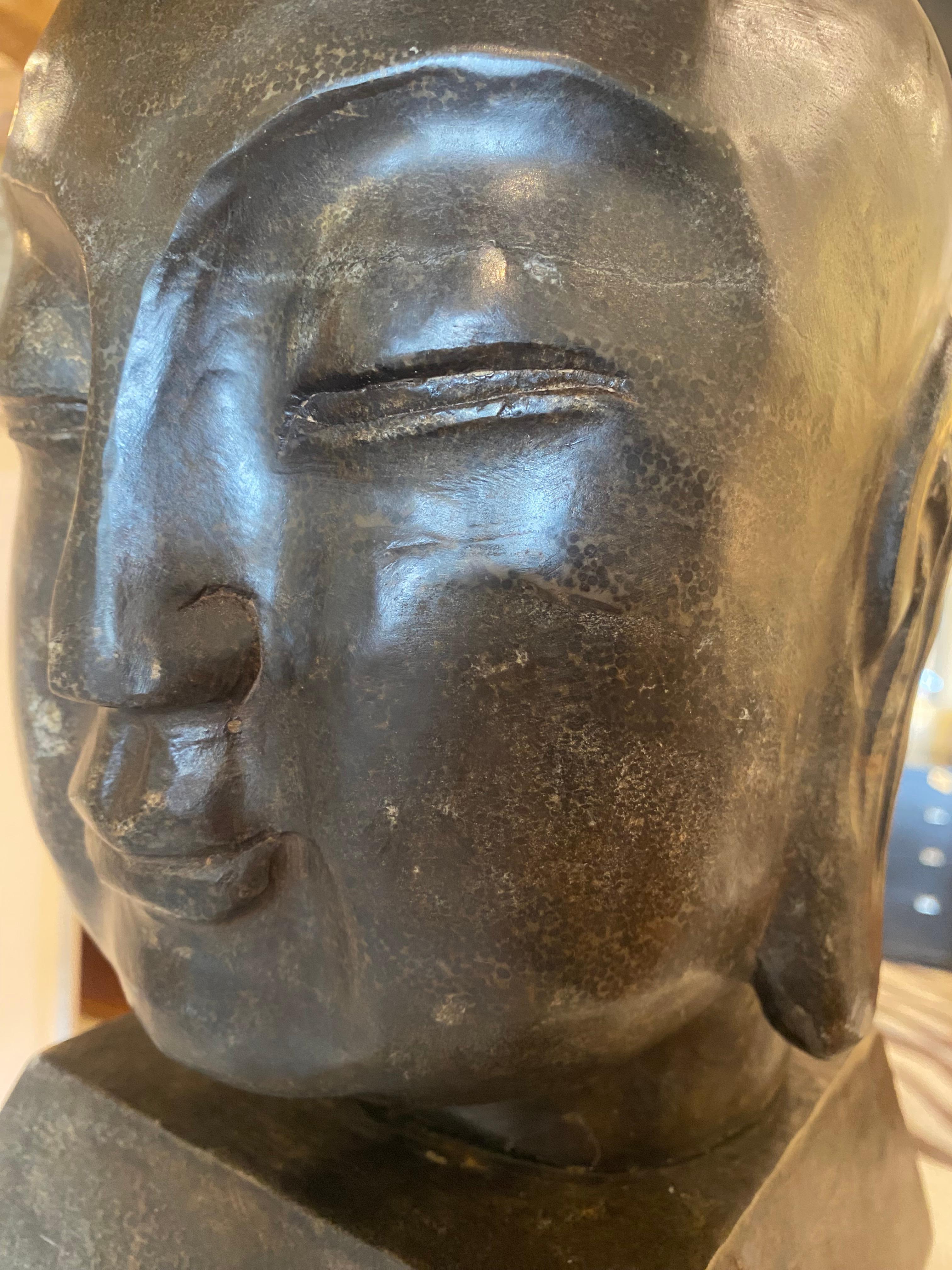 This sculptural head, crafted from heavy soapstone —a naturally occurring metamorphic rock —depicts a serene Southeast Asian-style figure with softly closed eyes, arched brows, and a gentle expression. The minimalist detailing and the smooth,