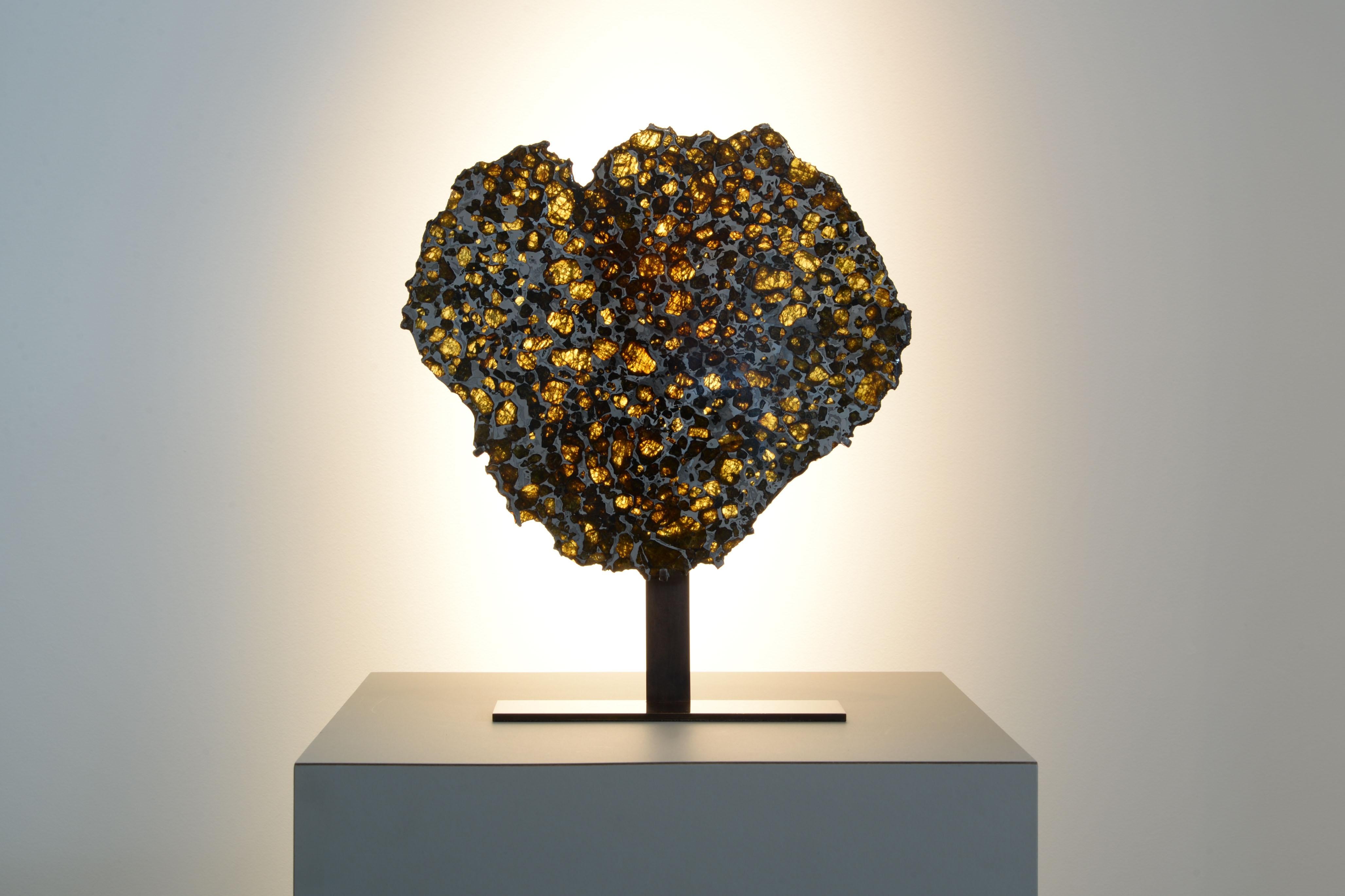 This complete cross-section from the pallasite meteorite Imilac has been prepared to reveal shimmering olivine and peridot gems embedded in iron-nickel metallic crystals, forming a magnificent honeycomb pattern characteristic of pallasites. Imilac