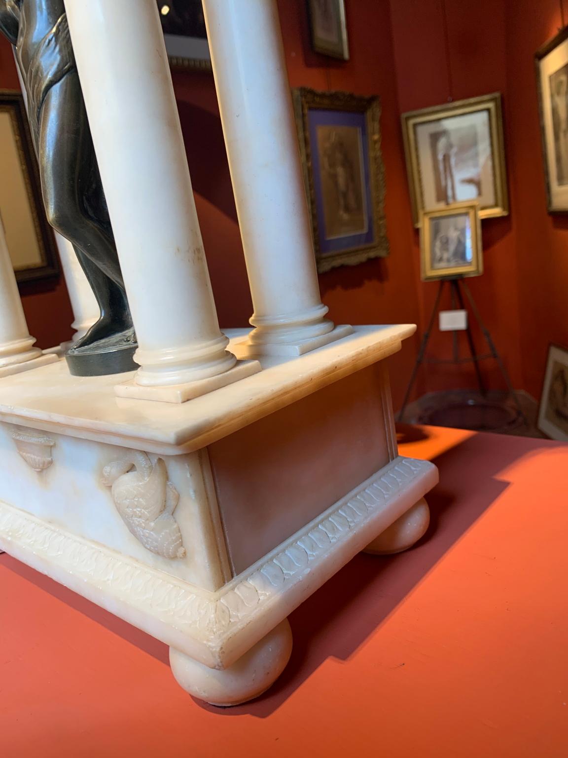 Templo de alabastro con capiteles corintios, decoración de palmeta en el borde. En la parte delantera, en la base, hay tallados dos cisnes, mientras que en la parte superior hay cinco rosetas.
En el centro hay una estatuilla de bronce que representa