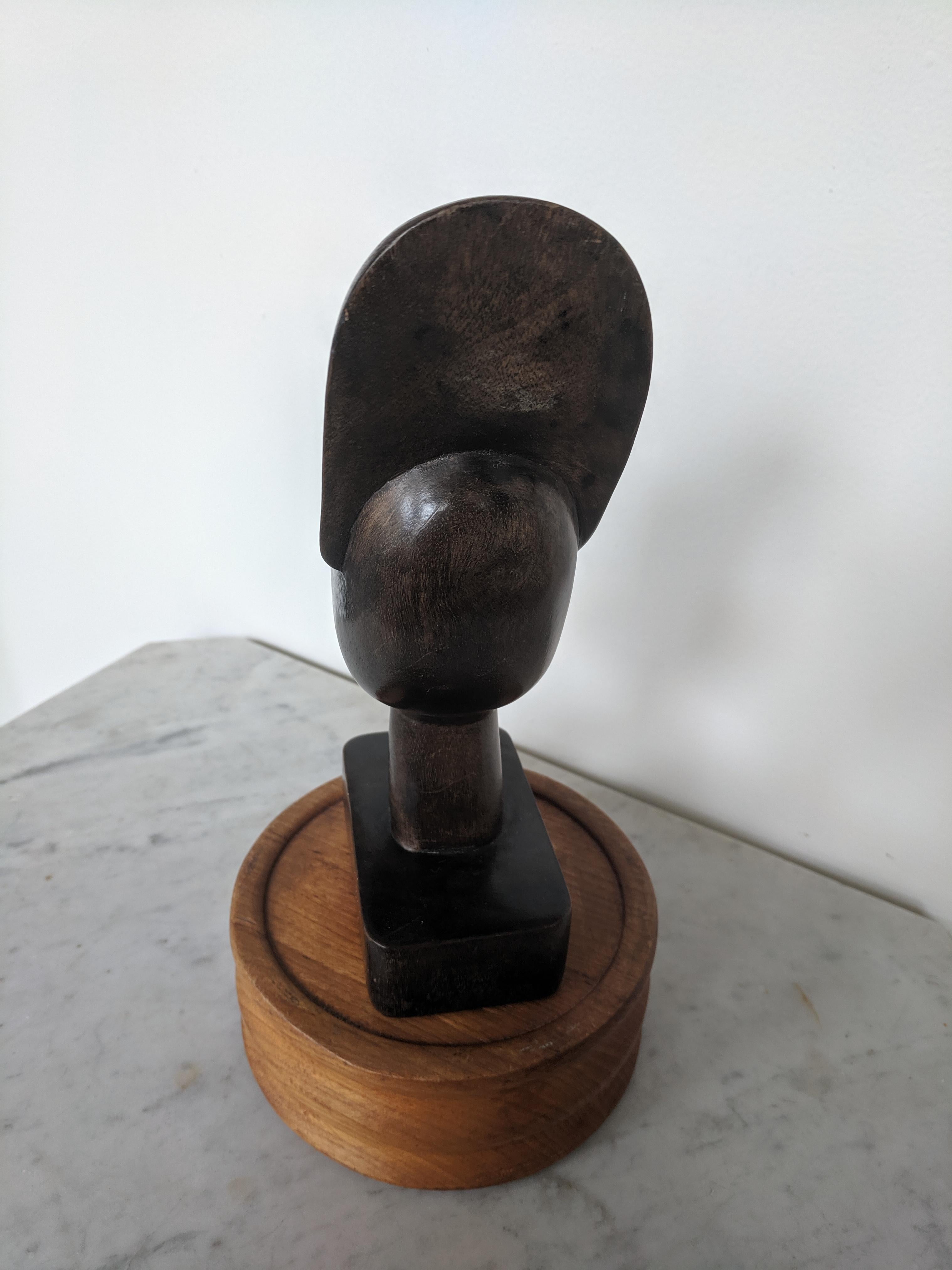 Dieser skulpturale Kopf wird in Haiti aus Mahagoniholz hergestellt. Das Holz hat eine abgenutzte, dunkelbraune Patina. Die Schnitzerei ist eher minimalistisch und verleiht einer Stammesgeste eine moderne Note. Der Kopf ist unten mit 