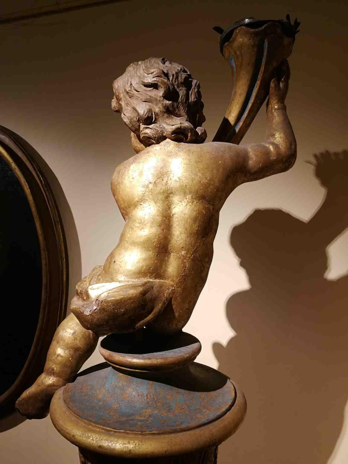 One flame candle holder putto made of gilded wood.
Those kind of objects were present in churches or noble villas, specially during the Baroque times. 

The base is not coeval.

