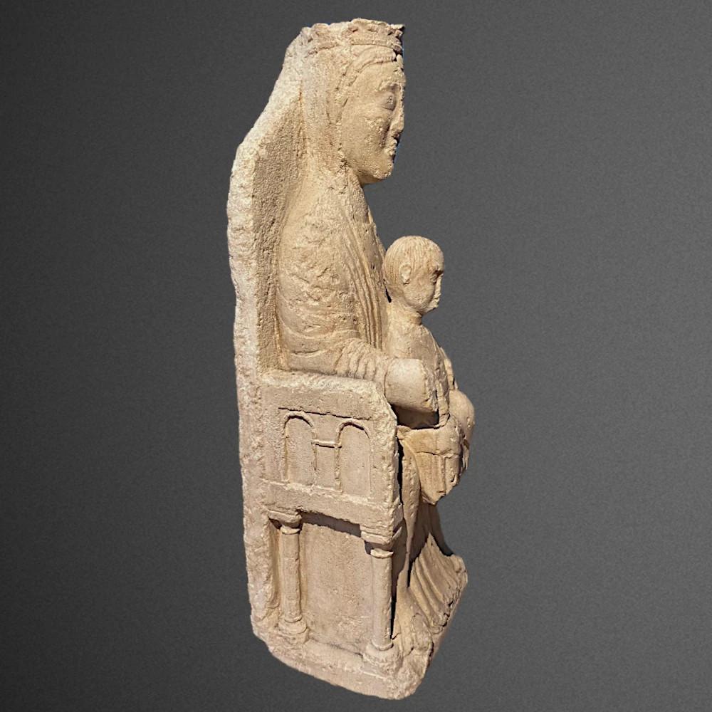 Rara Vierge romane en majesté en pierre calcaire sculptée en très haut-relief. La Vierge tient l'Enfant entre ses deux genoux dans une parfaite frontalité, une caractéristique des premières vierges romanes dites Sedes Sapientiae. Marie è circondata
