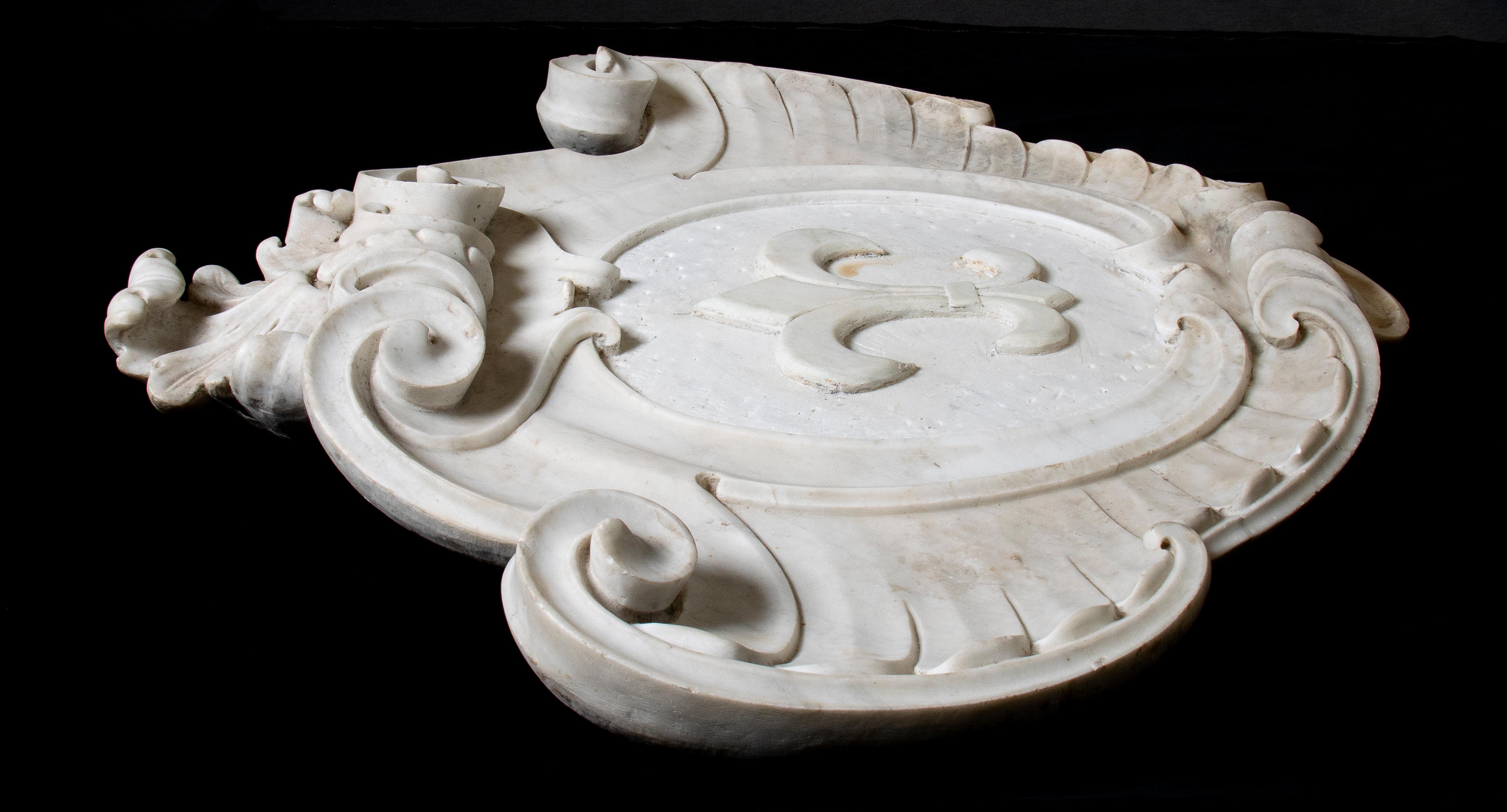 Un très intéressant Coates, sculpté en marbre blanc avec une structure symétrique et une décoration à double rouleau ainsi que des sculptures de feuilles d'acanthe. Avec représentation centrale d'une fleur de lys dans les armoiries.
La fleur de lis,