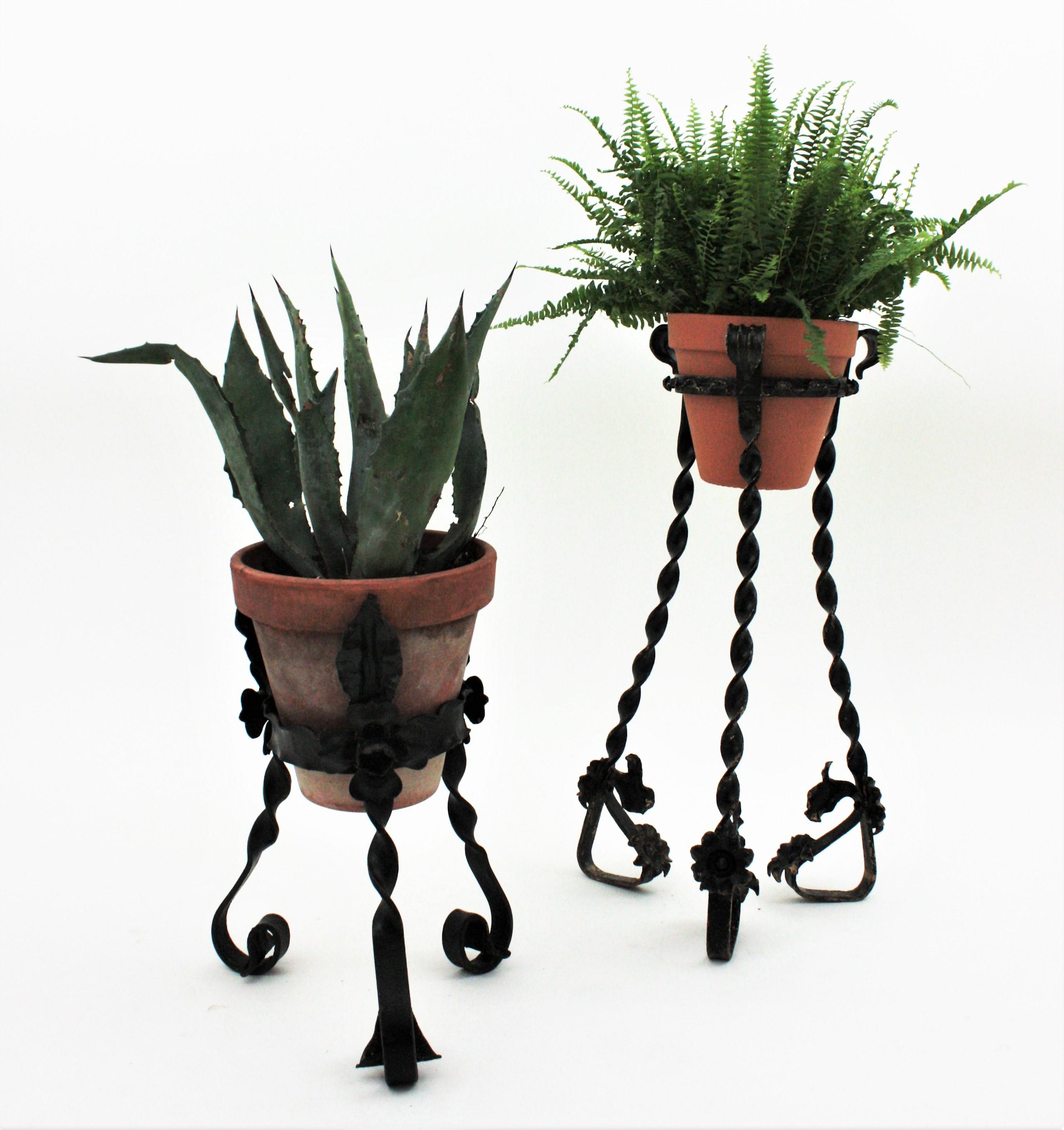 Eye-catching set of two tripod stands in wrought iron with foliage and floral motifs. Spain, 1930s.
The set is comprised by a taller plant stand and a shorter one. Both handcrafted in hand forged iron and standing on twisted iron bases with