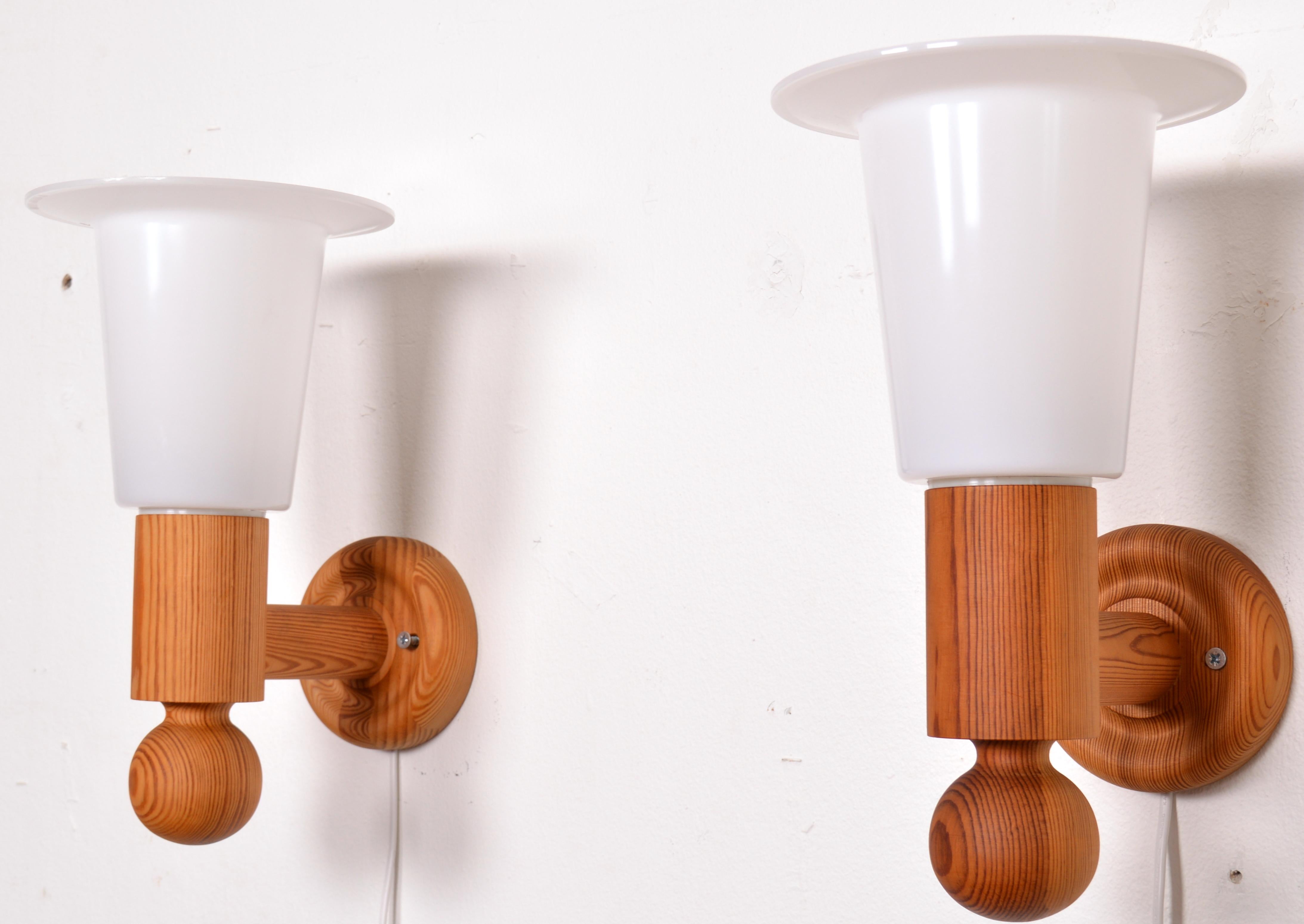 A pair of large wall lights designed by Uno Kristiansson circa 1966 and made by Luxus. The main body of the design is turned pine wood. White acrylic diffusers sit atop the sconces. Although the form of the lamps is curvaceous and their edges soft,