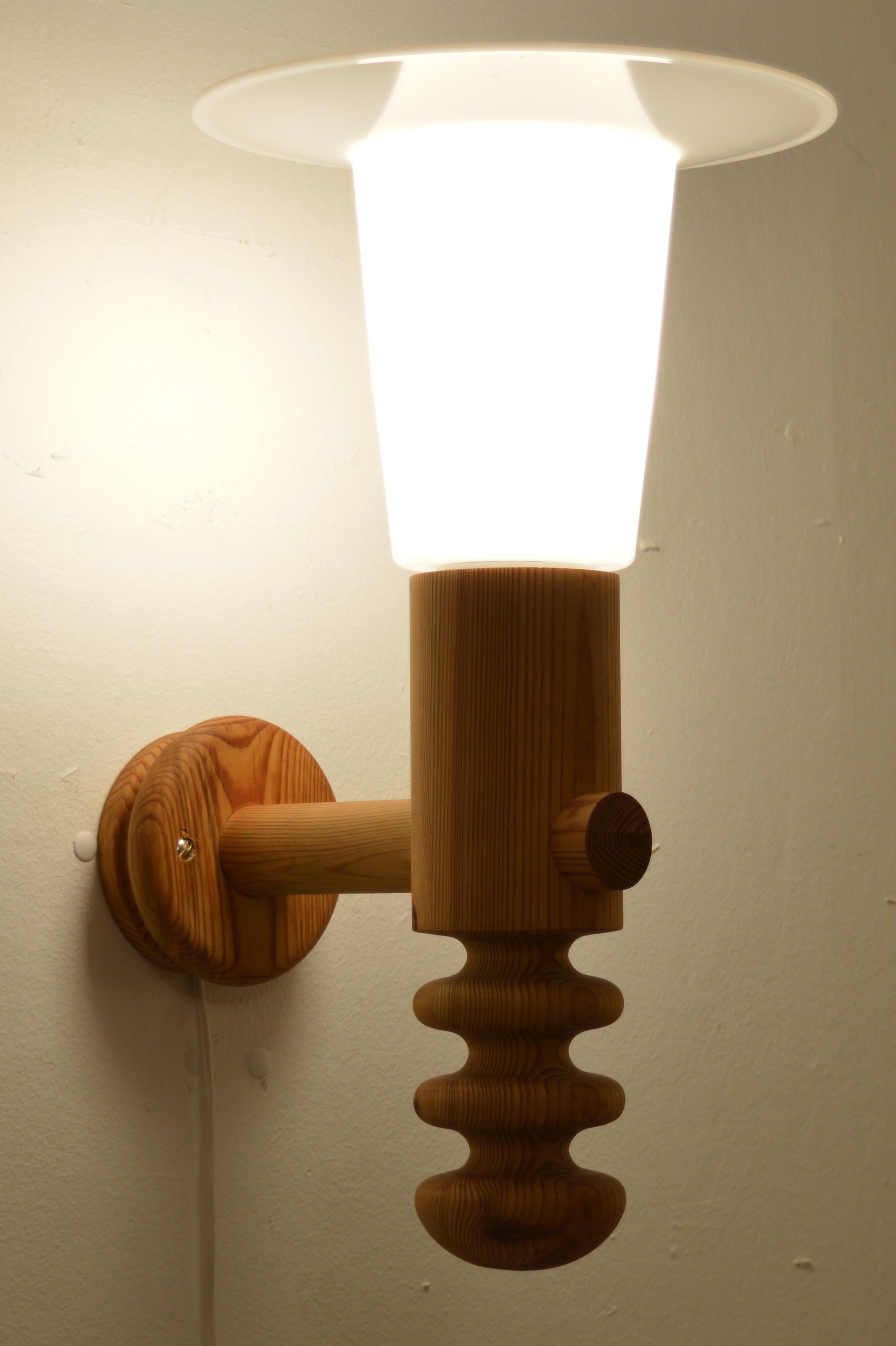 A large wall light designed by Uno Kristiansson circa 1966 and made by Luxus.The main body of the design is turned pine wood. White acrylic diffuser sit atop the sconce. Although the form of the lamp is curvaceous and their edges soft, the scale of