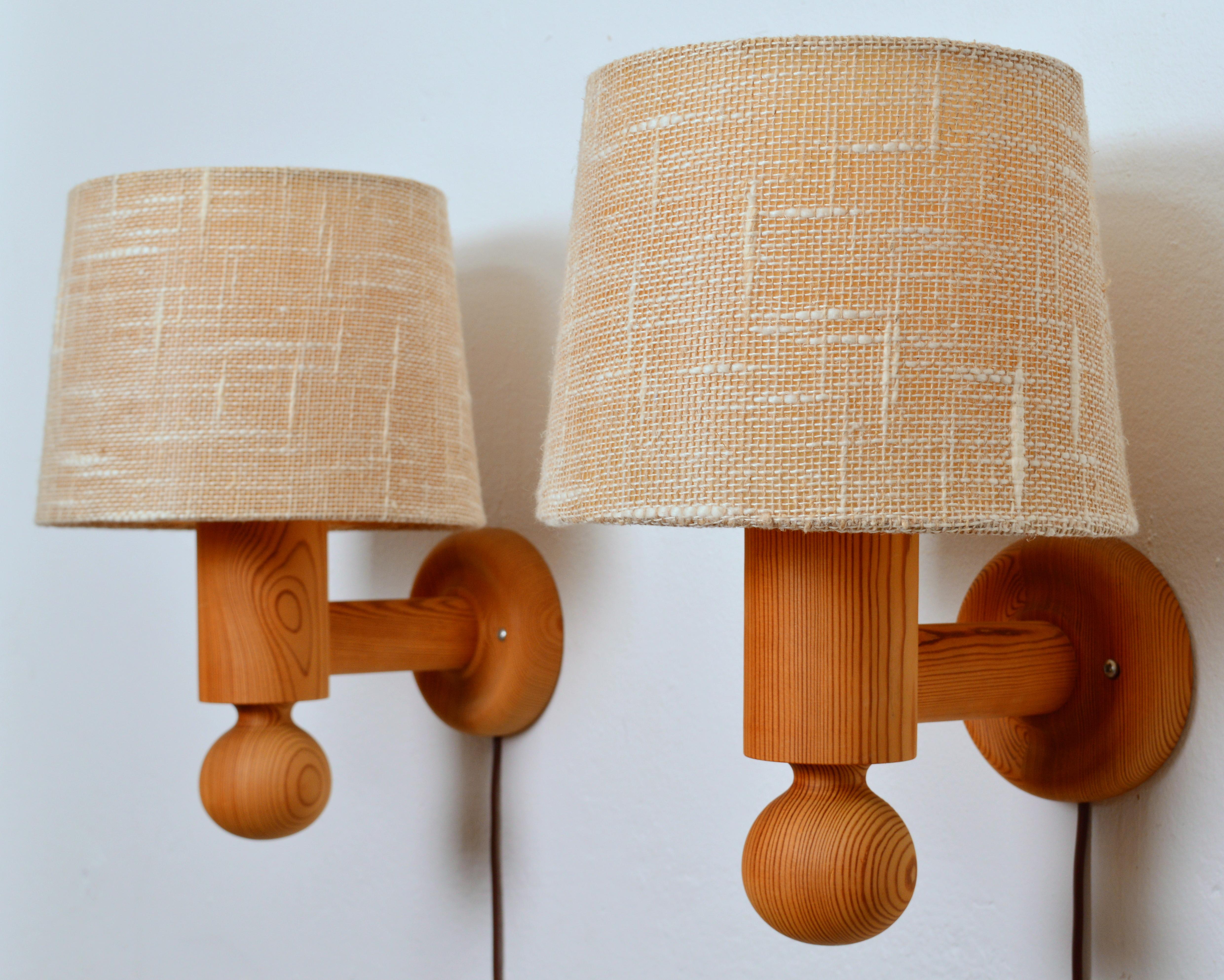 A pair of large wall lights designed by Uno Kristiansson circa 1966 and made by Luxus. The main body of the design is turned pine wood. White acrylic diffusers sit atop the sconces and fabric shades cloche the diffusers. Although the form of the