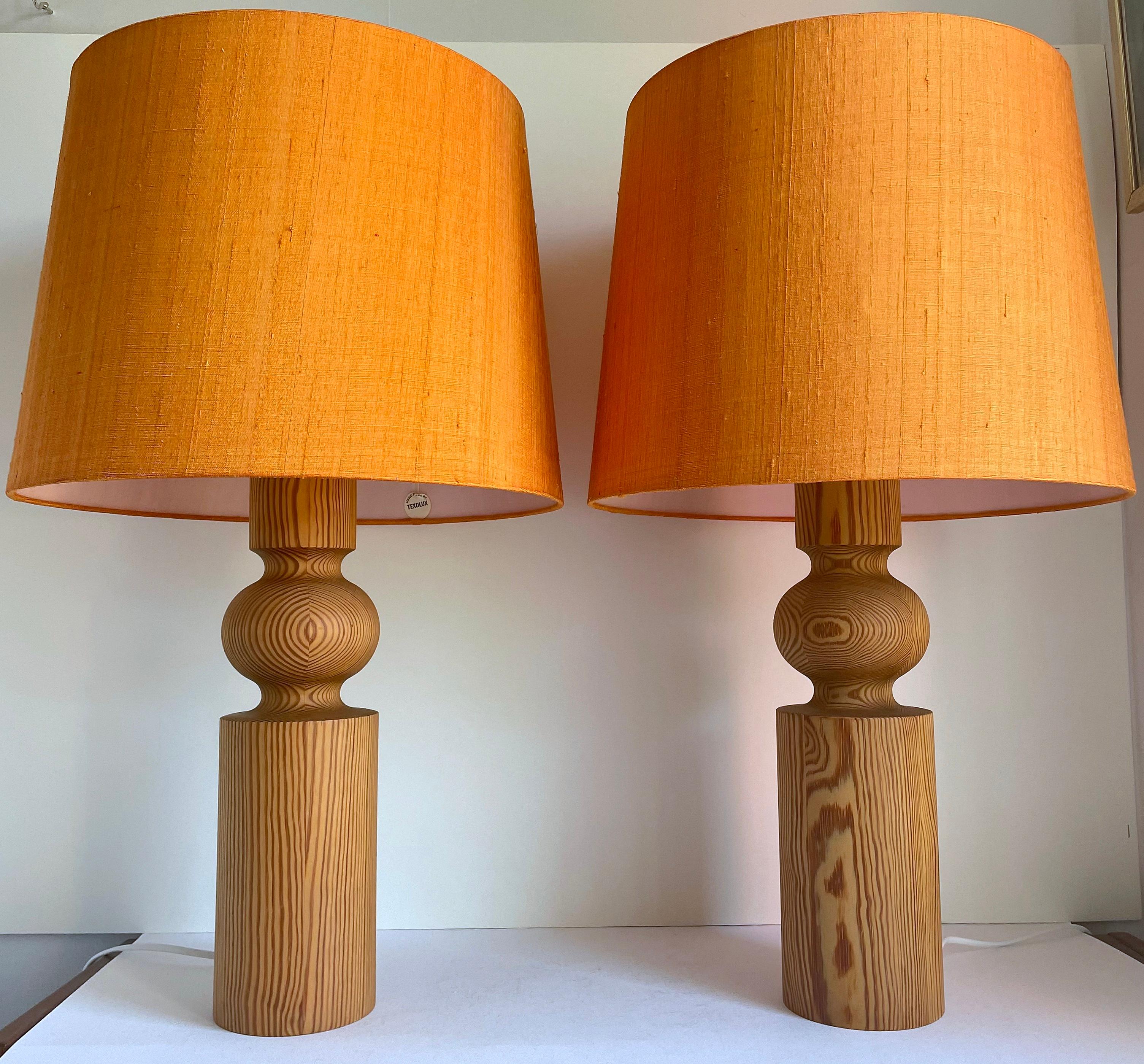 A pair of large, sculptural, solid pine table lamps designed by Uno Kristiansson around 1966 and made by Luxus. The  body of the design is turned pine wood. White acrylic diffusers sit atop the lamps and original Texolux orange fabric shades cloche