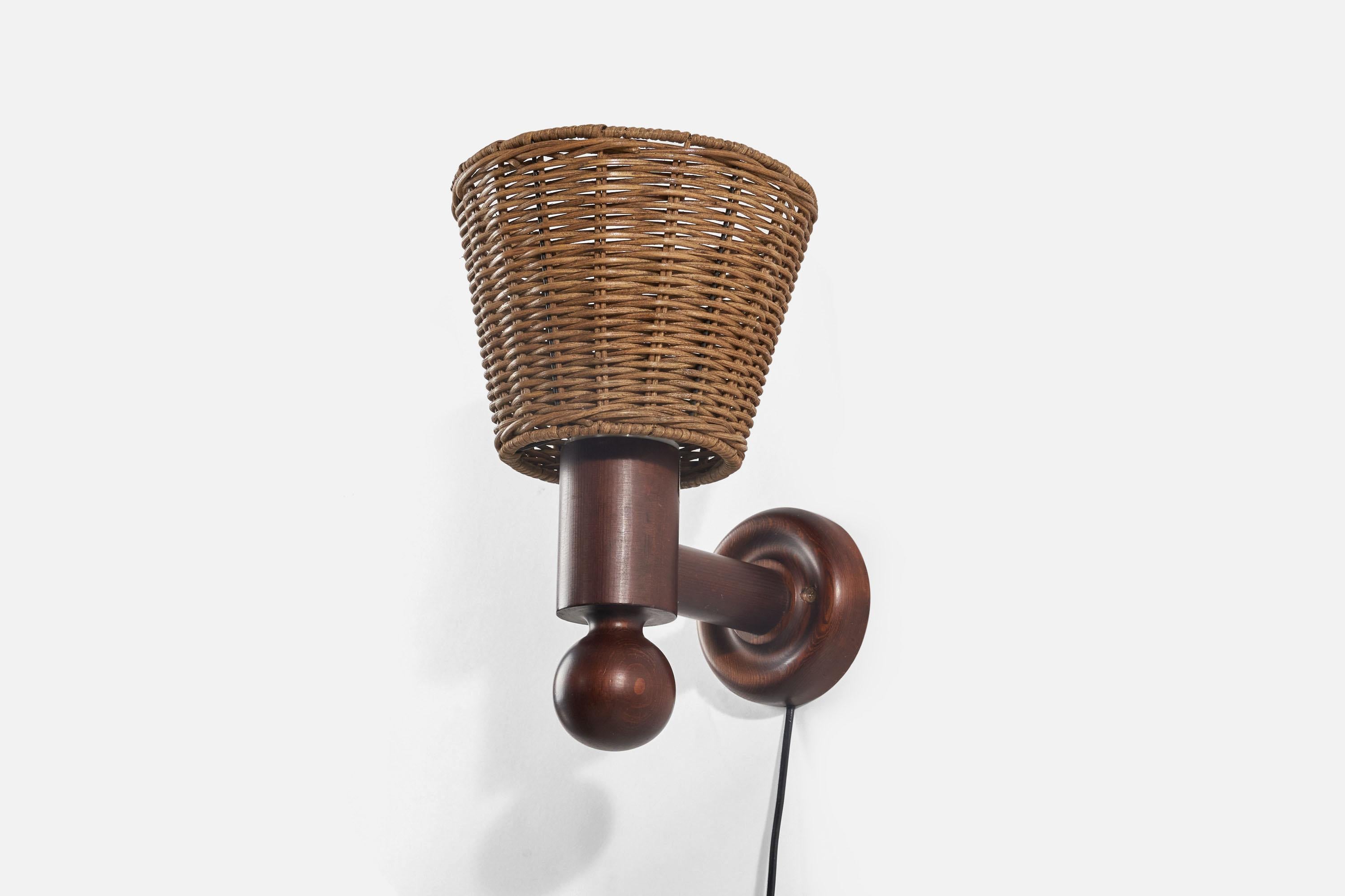 A dark-stained pine and rattan wall light designed by Uno Kristiansson and produced by Luxus Vittsjö, Sweden, 1970s.

Sold with Lampshade(s). Dimensions stated are of sconce with shade(s).

Dimensions of back plate (inches) : 4.75 x 4.75 x 1.13