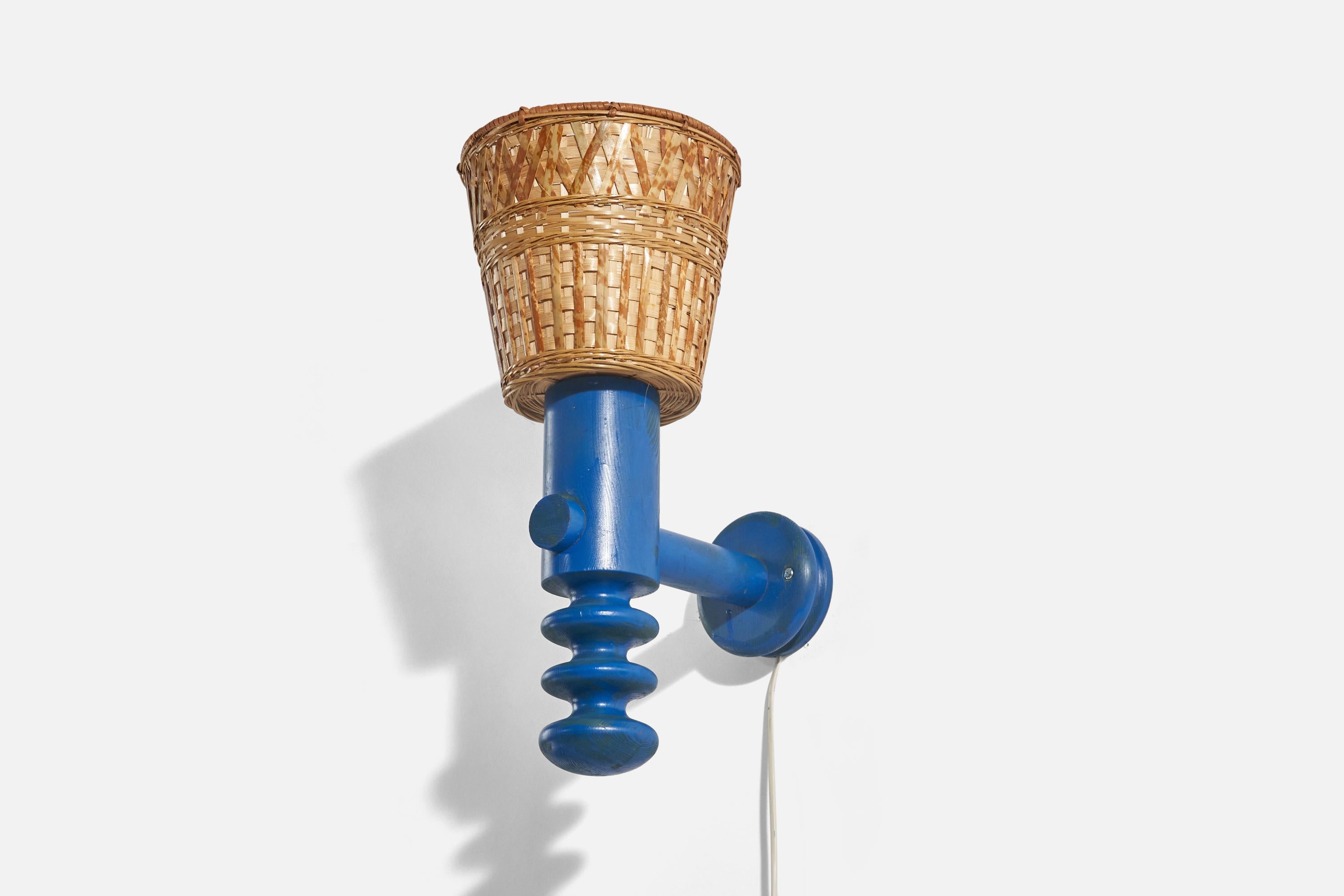 A blue-painted pine and rattan wall light designed by Uno Kristiansson and produced by Luxus Vittsjö, Sweden, 1970s.

Sold with Lampshade(s). Stated dimensions refer to the Sconce with the Shade(s).

Dimensions of Back Plate (inches) : 4.6 x 4.6