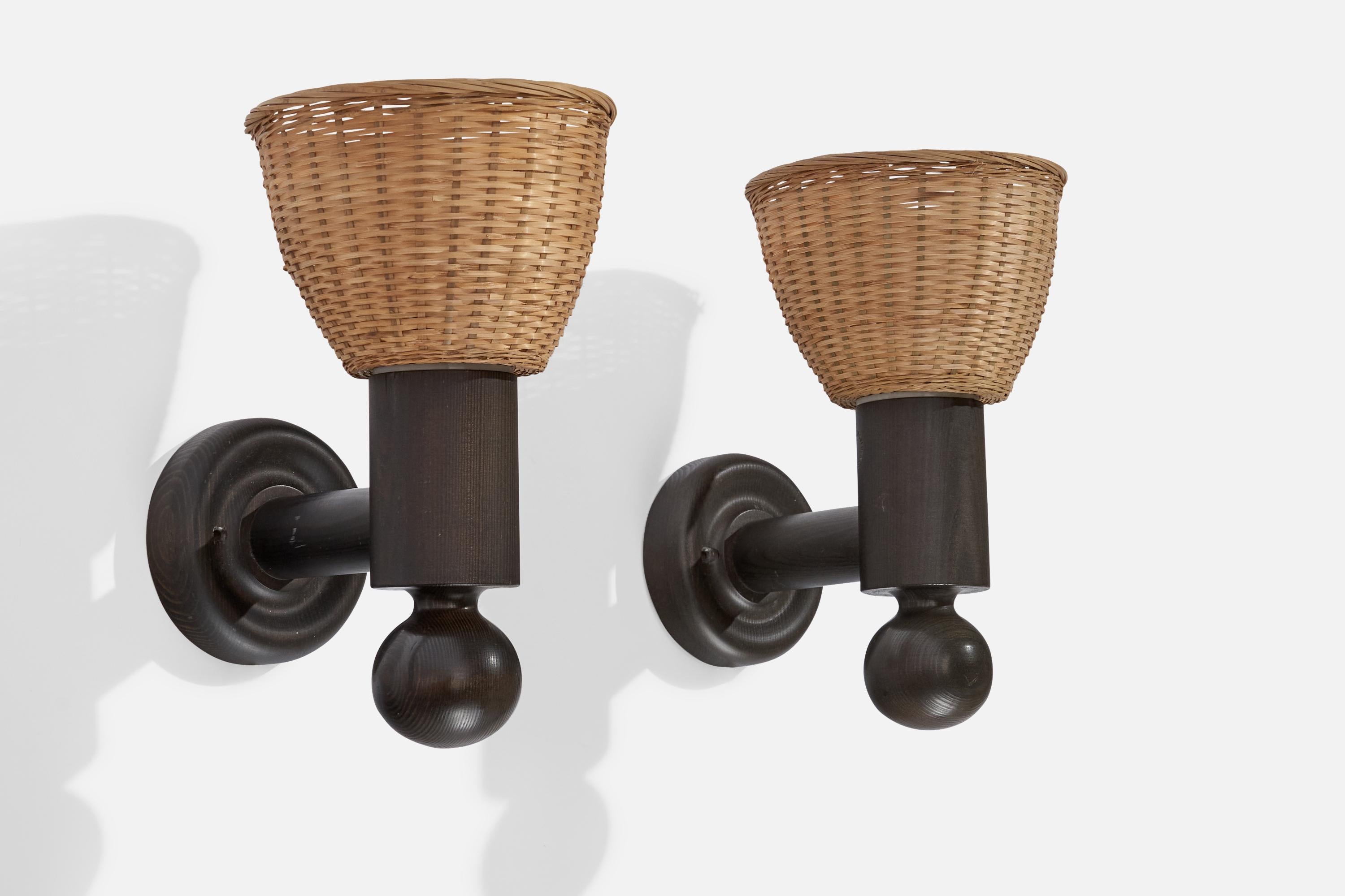 A pair of dark-stained pine and rattan wall lights designed by Uno Kristiansson and produced by Luxus, Sweden, 1970s.

Overall Dimensions (inches): 11.75” H x 6.75” W x 9” D
Back Plate Dimensions (inches): 4.73” H x 1.17” D
Bulb Specifications: E-26