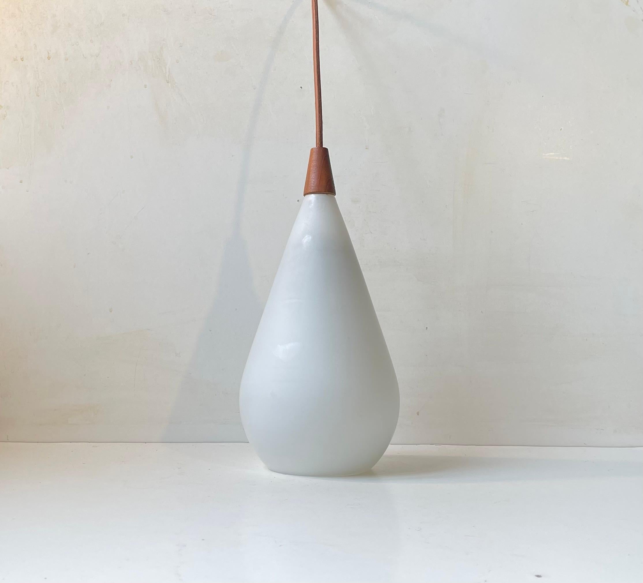 A simple Swedish Modern pendant light constructed of a blown matte opaline glass and a stylish top in solid teak. Designed by Uno and Ôsten Kristiansson and manufactured by Luxux in Sweden circa 1960-65. The lamp features a new brown textile cord.