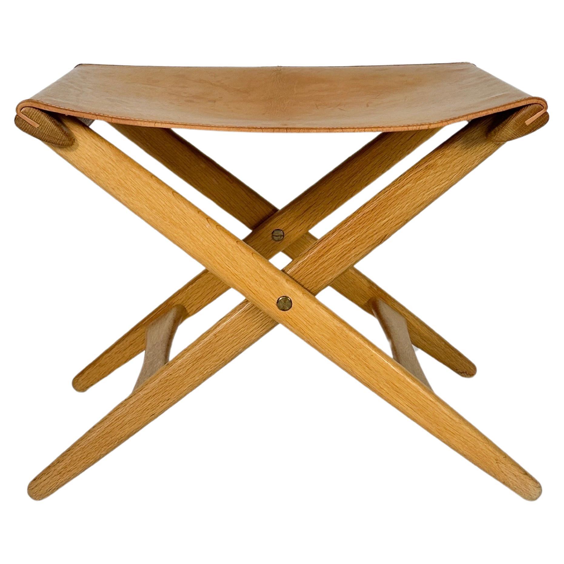 Rare folding stool designed by Uno & Östen Kristiansson for their own firm Luxus in Vittsjö, Sweden in the 1950s.

Solid oak with original leather seat.

Very good condition for its age. The leather has a few cracks along the seam, which does not