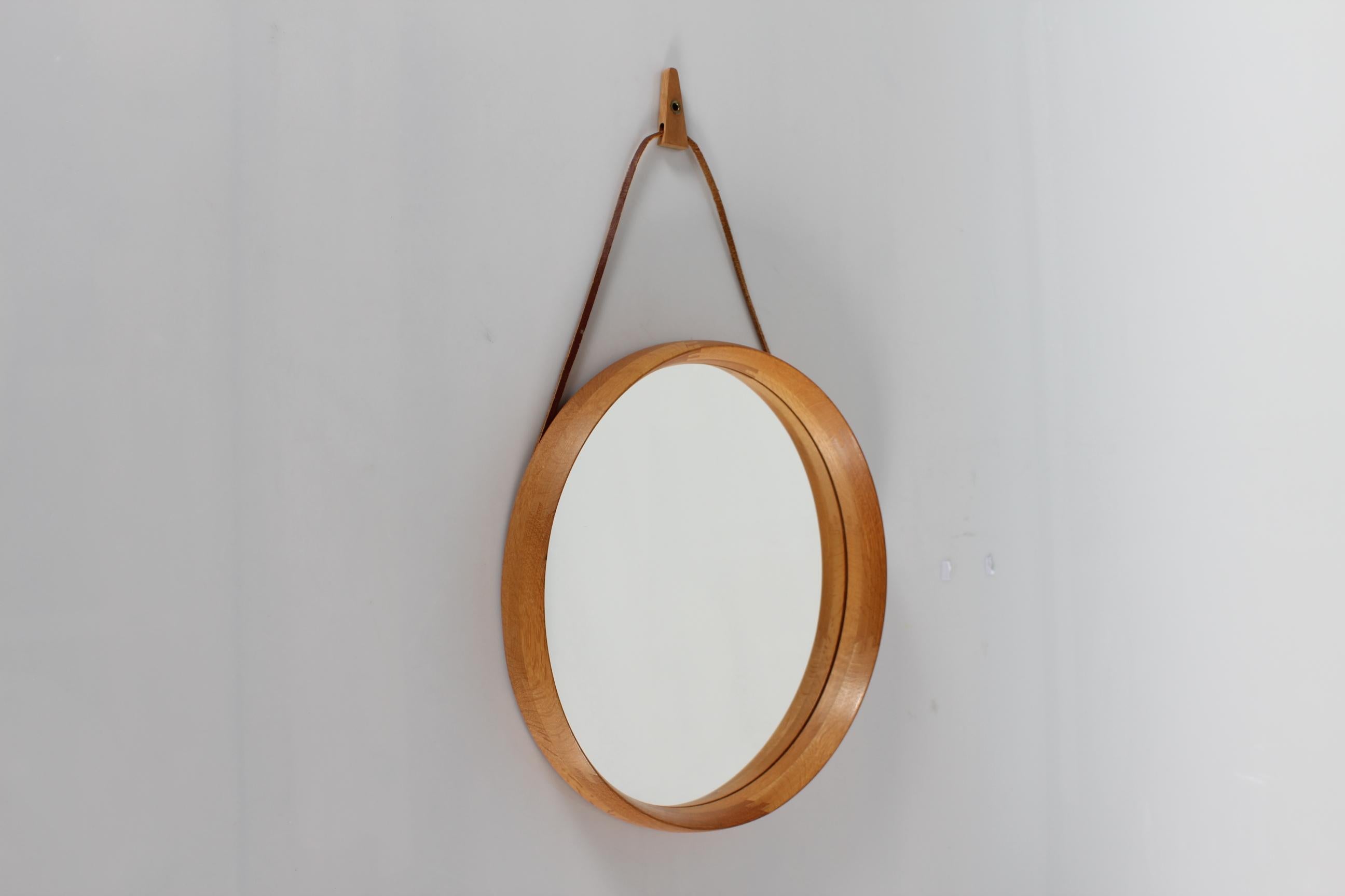 Uno and Osten Kristiansson round wall mirror made of solid oak by Luxus Vittsjö in Sweden in the 1970s. 
The mirror is made of solid oak with visible joints and a light fitting frame.
A small piece of oak wood is mounted on the leather strap for