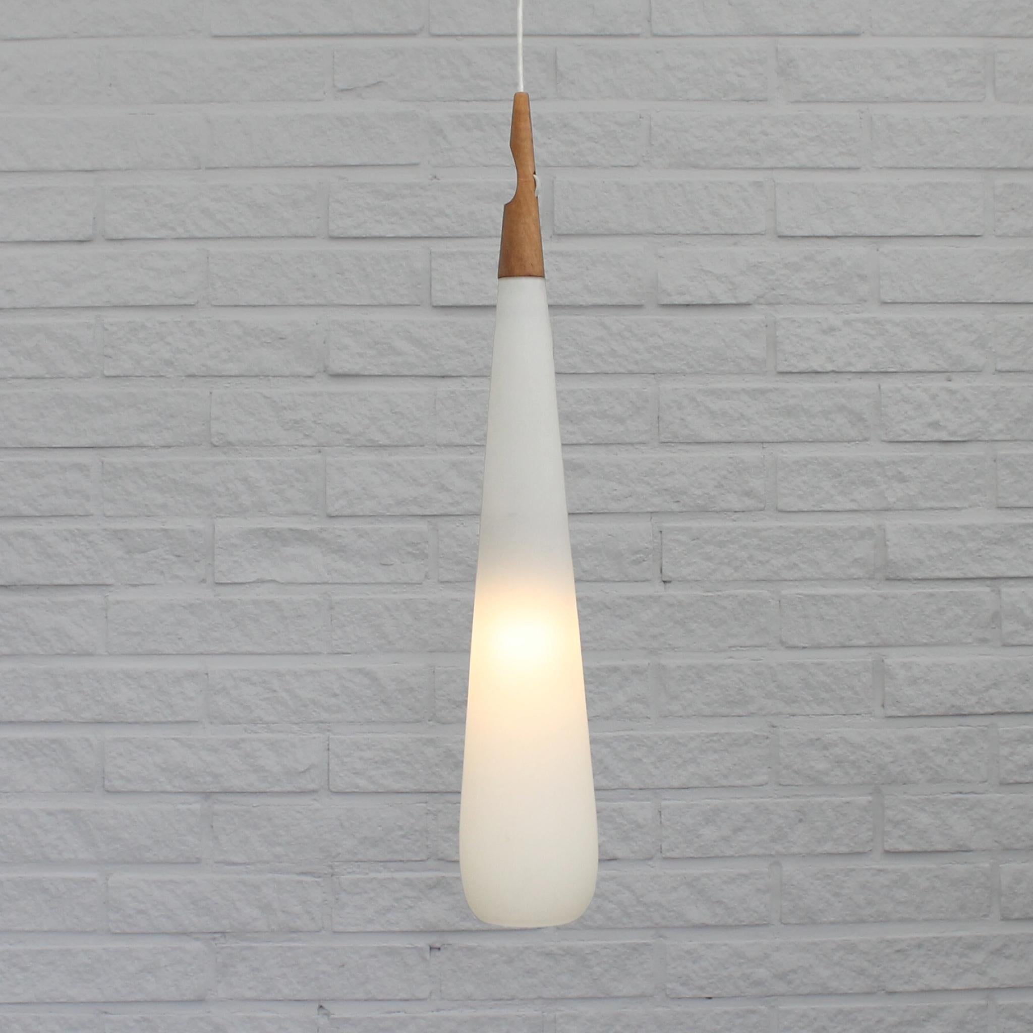 Large drop-shaped pendant lamp, model 546 ‘Baton’, designed by the Swedish brothers Uno & Östen Kristiansson for Luxus in Vittsjö. It features an elongated opaline glass shade and a wooden fixture with an integrated cable shortener. This oversized