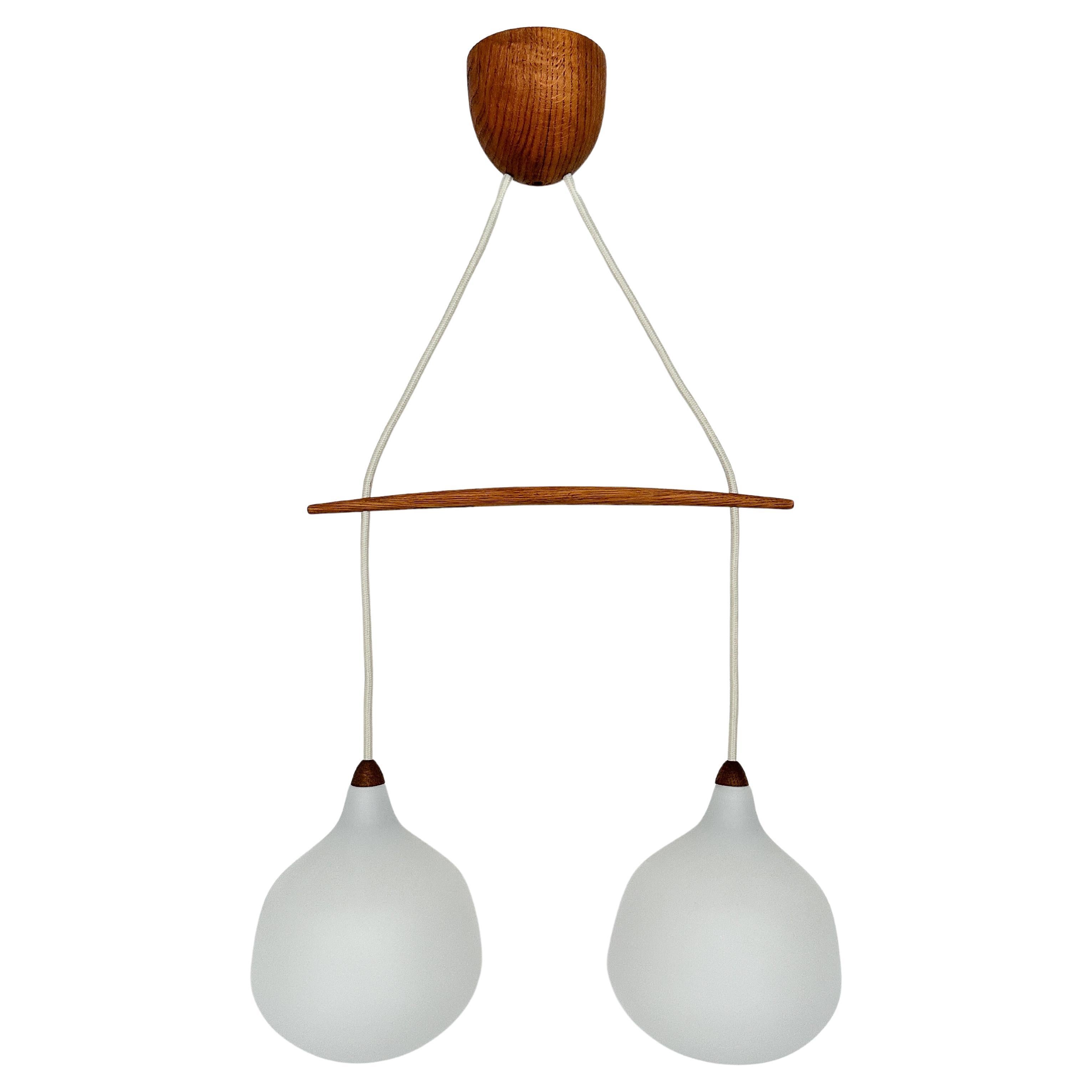 Uno & Östen Kristiansson double pendant lamp in oak and glass, produced by Luxus in Vittsjö Sweden, late 1950s.

The height of the wooden bar can be adjusted.

Very good condition with new fabric cords, remains the original manufacturers sticker on