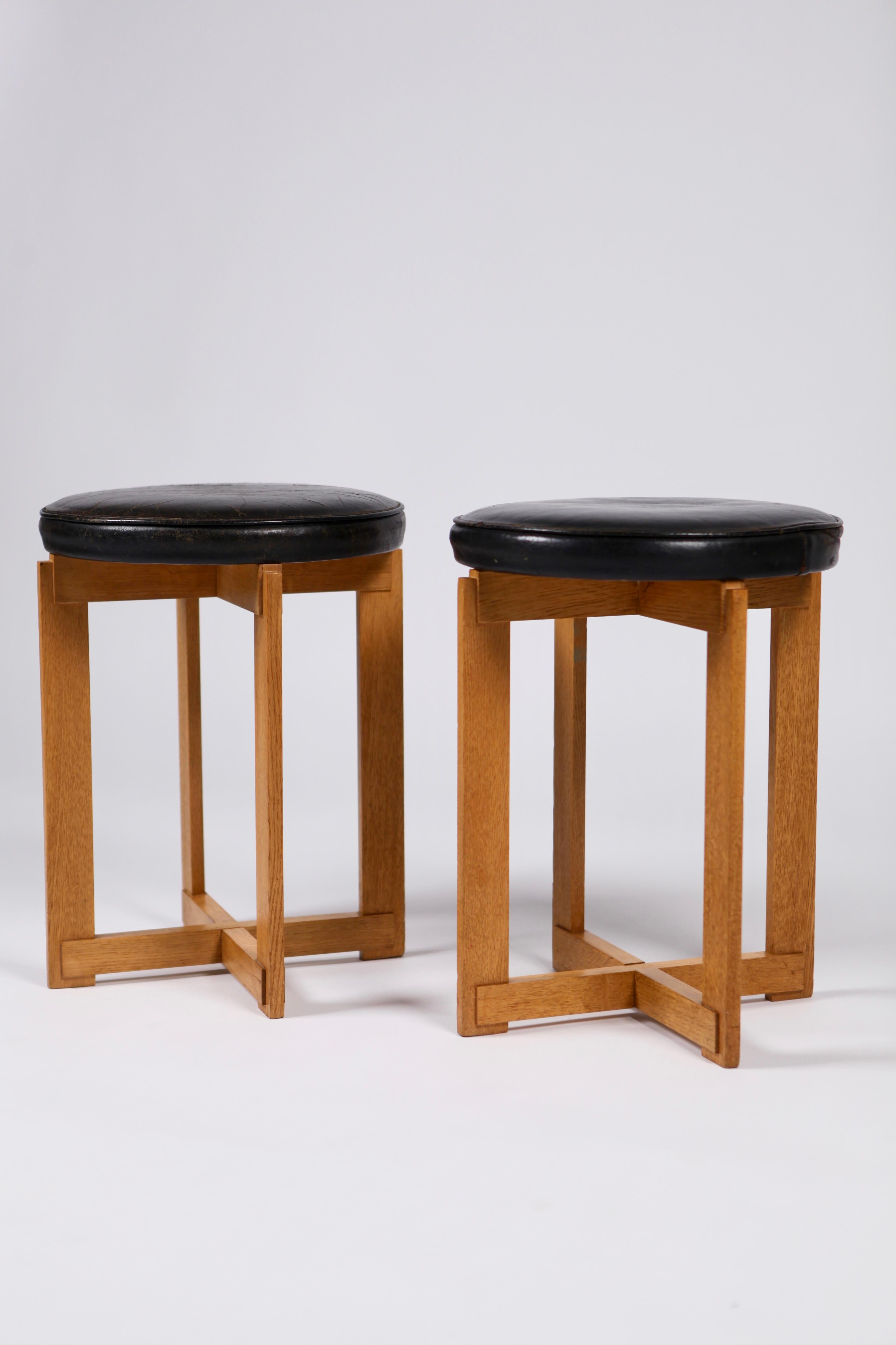 A pair of rare black leather and oak stools by Uno & Östen Kristiansson for Luxus, executed in Sweden in the 1960s. Sculptural base and padded seats, original leather (one stool with a small break in the leather), with wear and nice patina to the