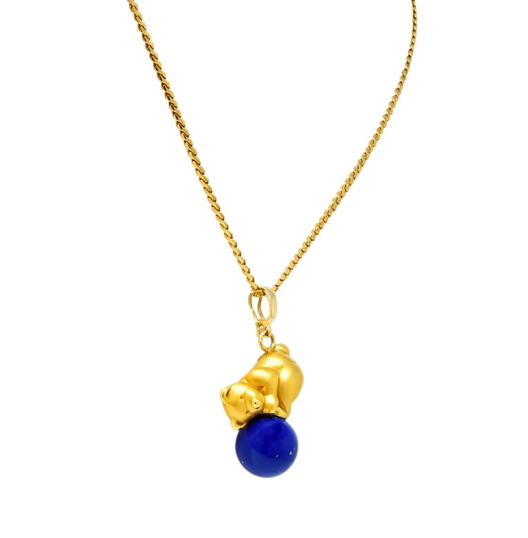 With a matte and polished gold teddy bear

Bear holding a round polished lapis lazuli bead, bright blue with flecks of pyrite measuring approximately 12.1 mm

With a 14 karat gold hinged bale

Accompanied by 18 karat gold serpentine style chain,