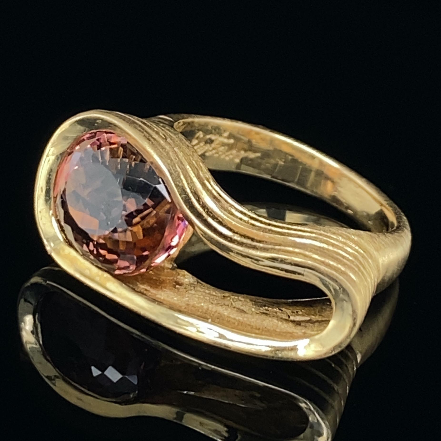 This gorgeous, freeform ring in satiny 18 karat yellow gold by Eytan Brandes features a 6.3 carat pink tourmaline with a luscious brown undertone.  

The mixed cut, oval-shaped tourmaline is from Mozambique.  This stone, including that amazing