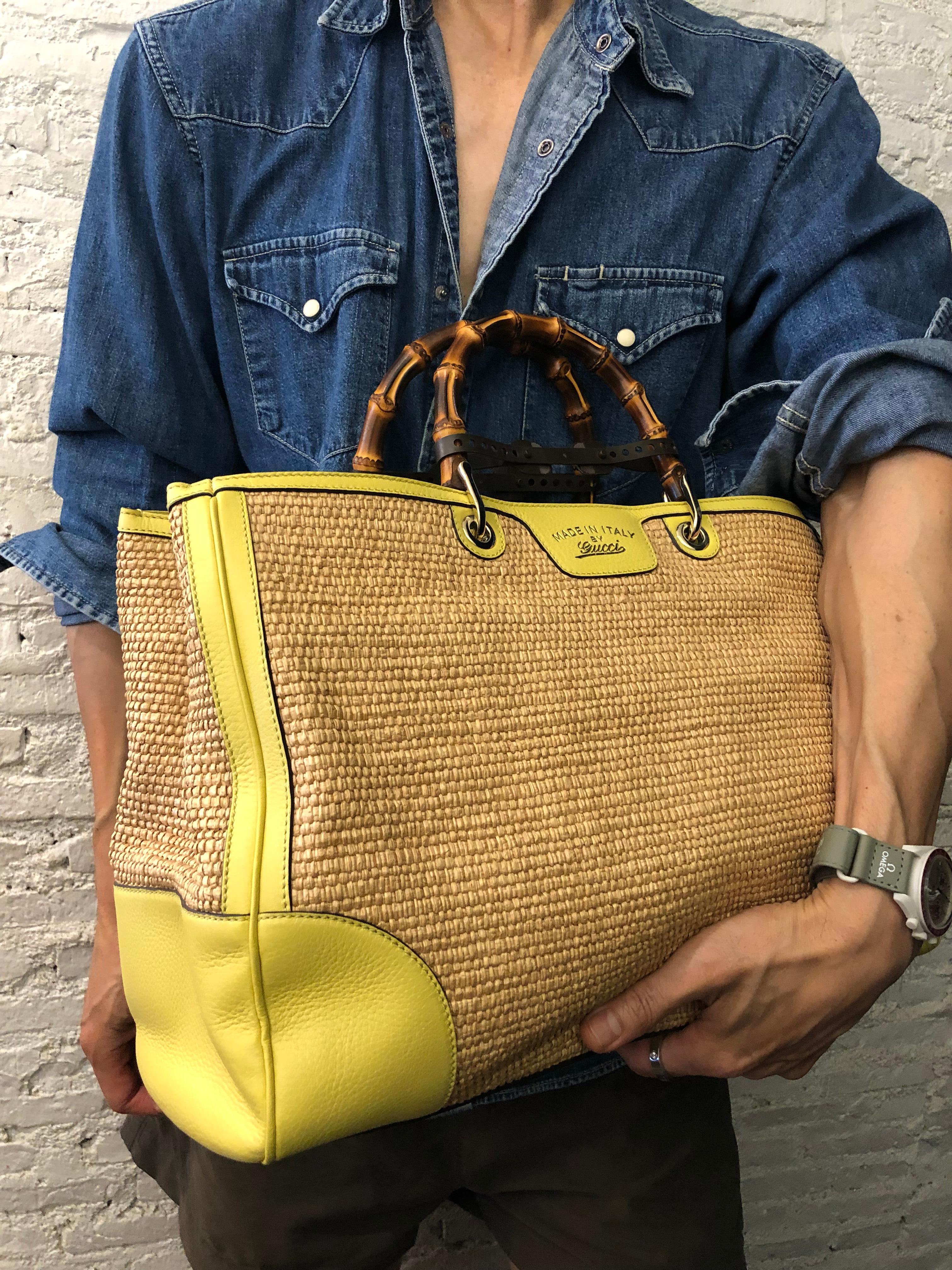 This large GUCCI raffia bamboo tote bag is crafted of woven straw in its natural color with yellow calfskin leather featuring gold toned hardware and sturdy bamboo handles. Wide top magnetic closures open to a striped canvas interior featuring two