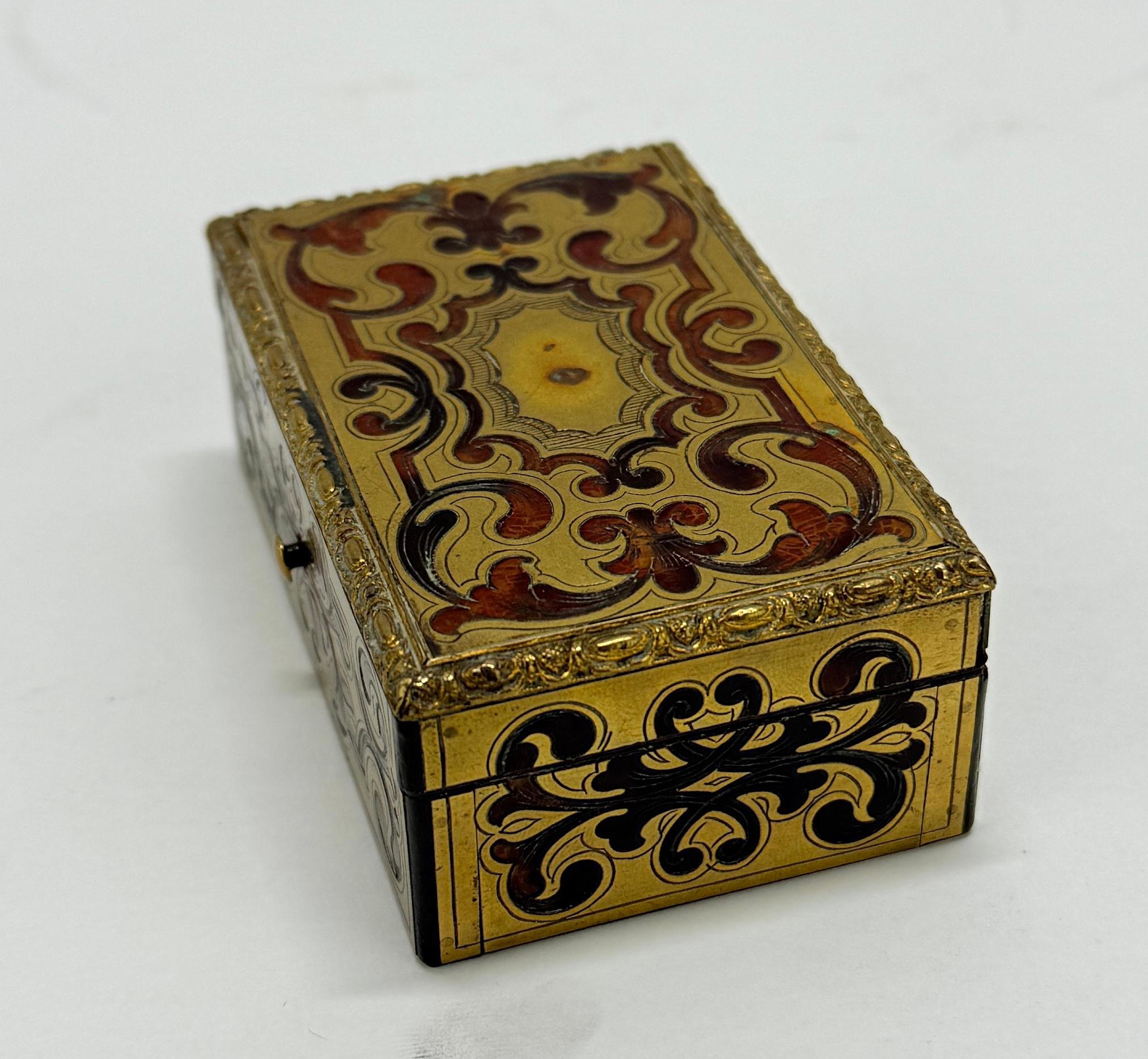Cette tabatière française du XVIIIe ou XIXe siècle, à la fois petite et opulente, est un exemple du style Boulle, réputé pour sa décoration complexe en laiton doré et incrusté sur une base en écaille de tortue. Mesurant 3,375 pouces de large, 2,25