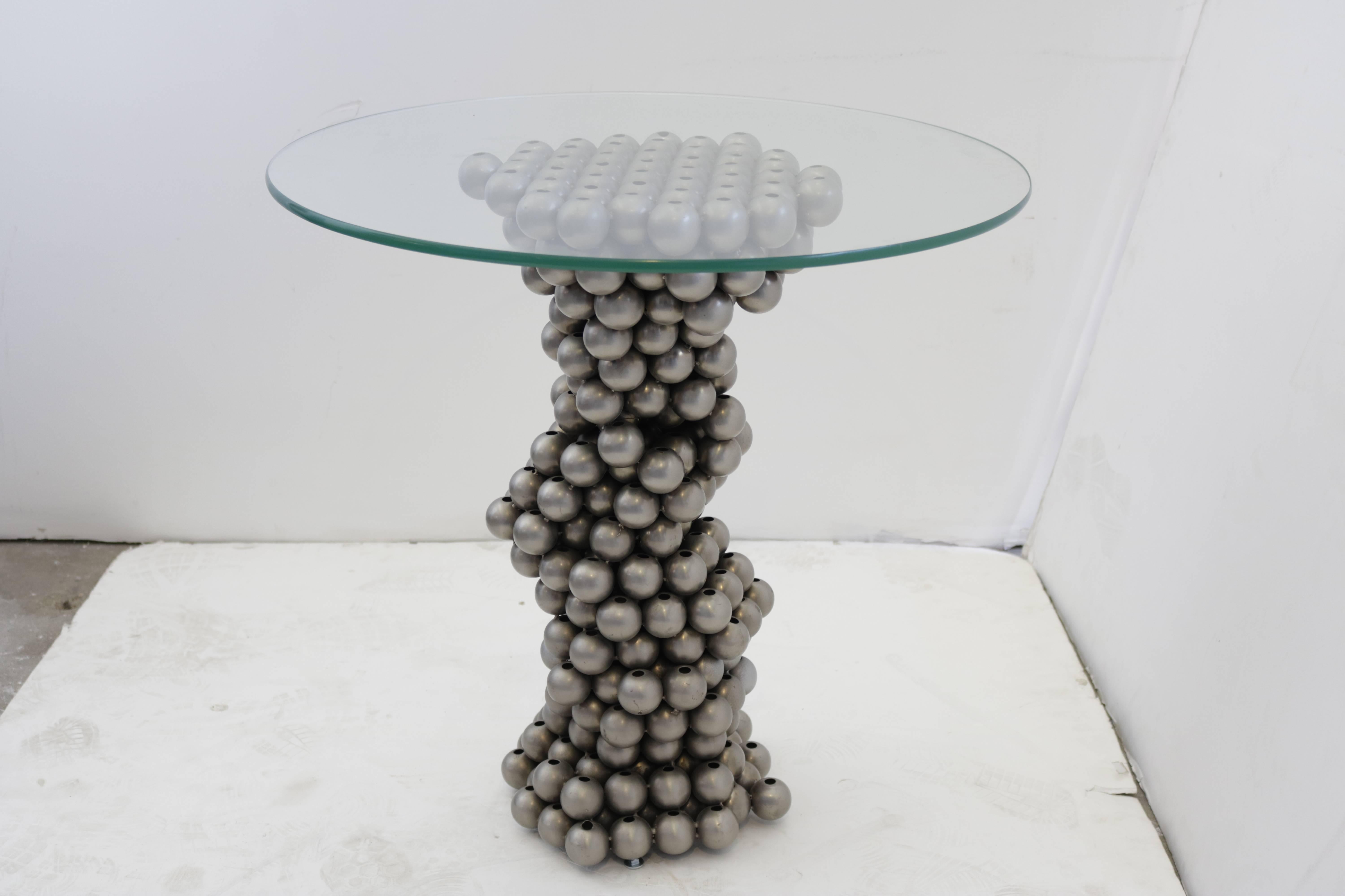 Unusual 1970s gueridon has a base made of chrome steel balls which resembles a spiral or helix. Glass top measures 24
