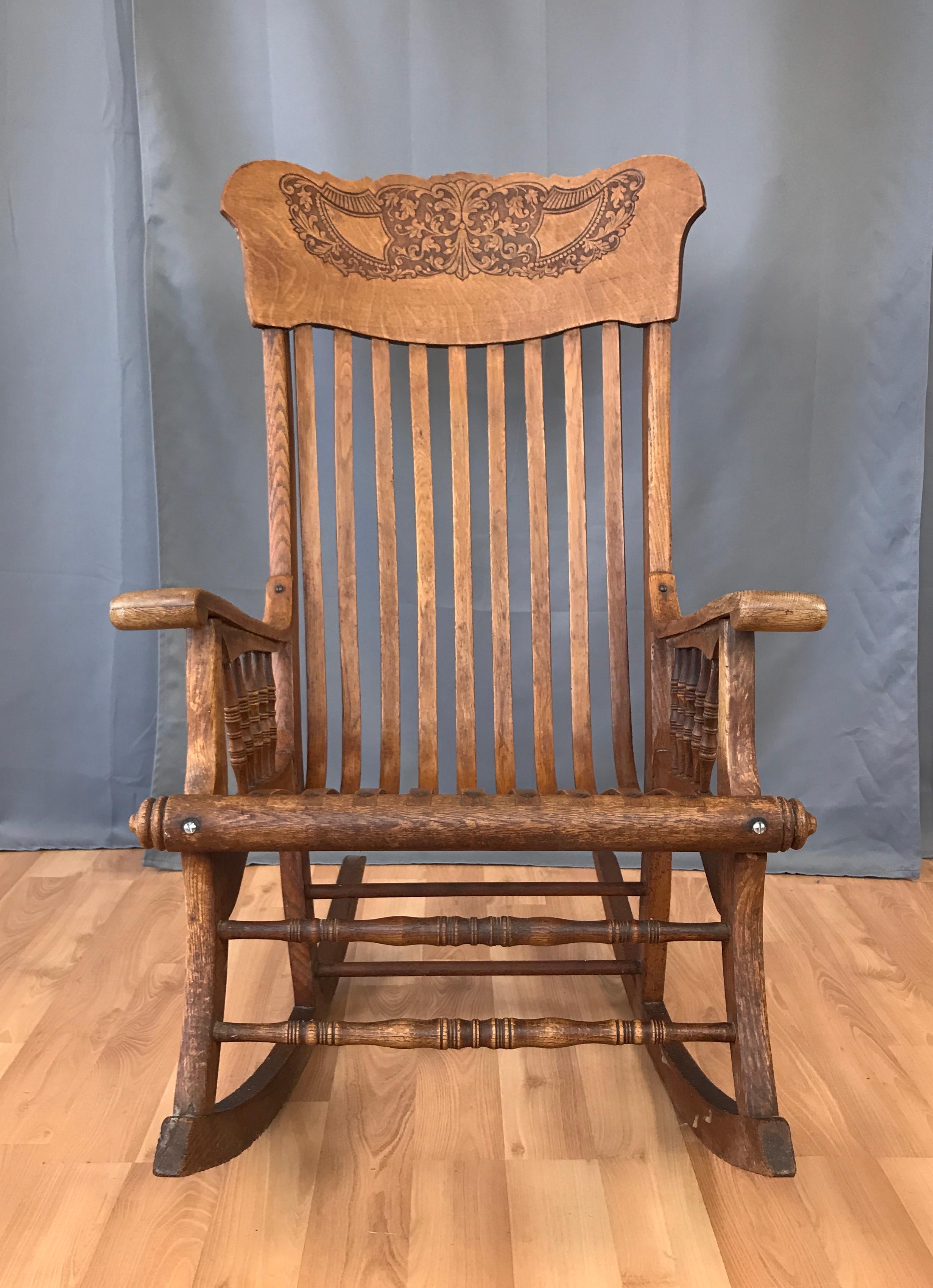 Unusual early 20th century rocking chair is solid oak. It features Victorian style spindles and bent quarter sawn oak head rest with a leaf motif. The seat and back is comprised of bent oak slats that attach to the frame with brass hardware. Well