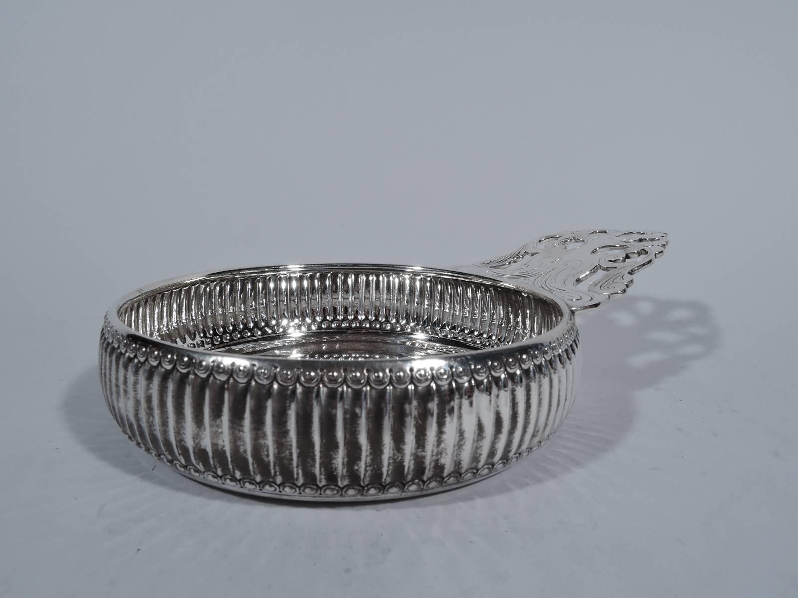 Unusual sterling silver porringer. Made by Tiffany & Co. in New York, circa 1883. Sides fluted between egg-and-dart borders. Open tree handle heightened with fluid engraving. Hallmark includes pattern no. 7519 (first produced in 1883) and director’s
