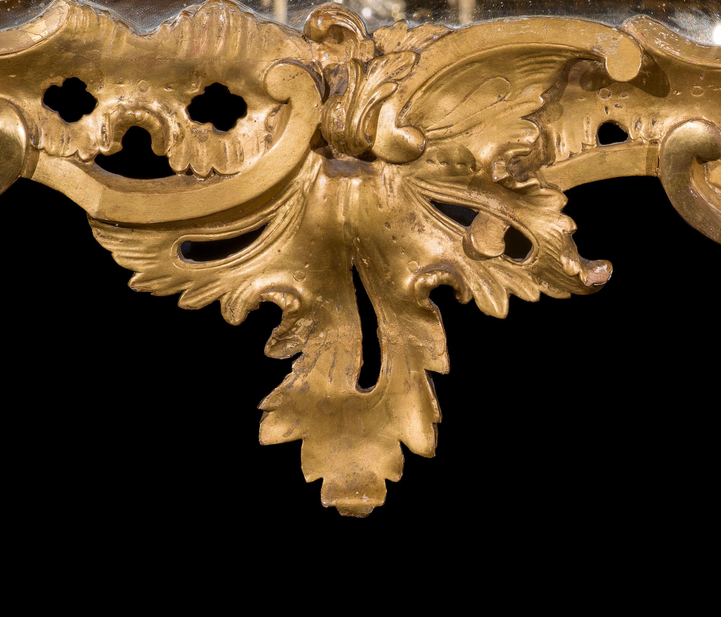 A very unusual George III Rococo wall mirror. The giltwood frame is carved with a wonderfully organic design, with foliate flourishes, trailing flowers and fruit, but the most unusual detail being the asymmetrical interlocking c scrolls to the lower