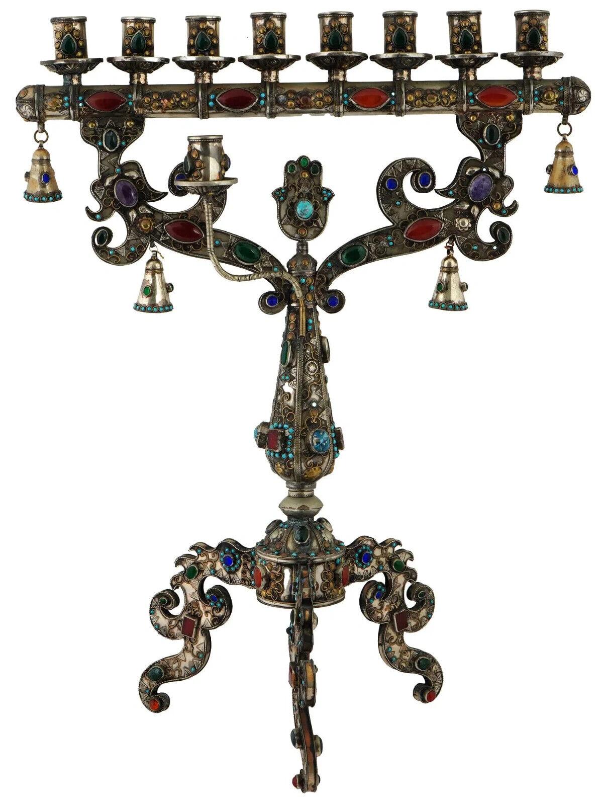 A vintage Turkmen manner copper and silver menorah decorated with gemstones and filigree. The menorah includes nine candle holders arranged in a curved design. The menorah features detailed filigree patterns, and adorned with colorful gemstones. The