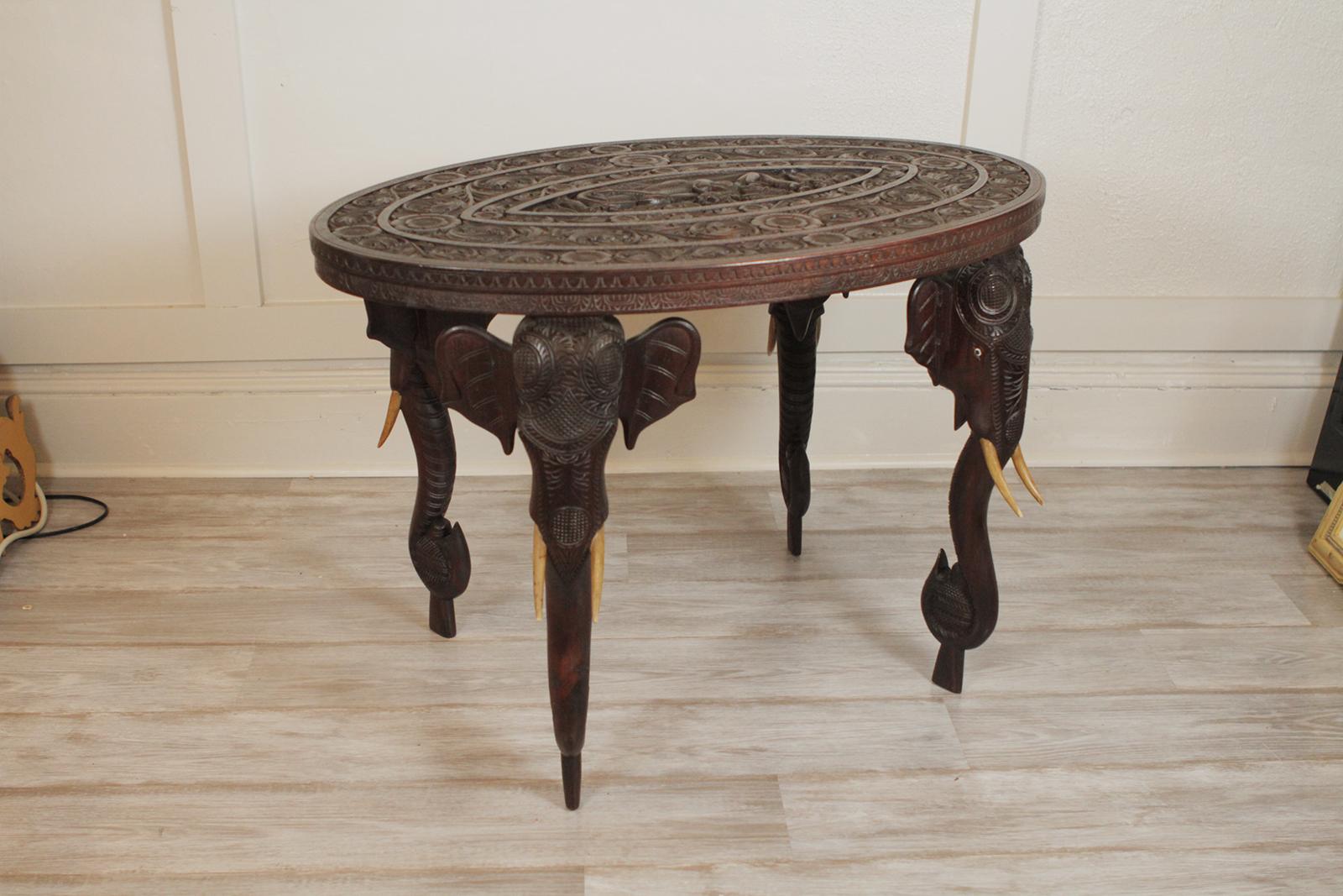 Exceptional quality hand-carved Anglo-Indian oval low table with elephant motif legs. The top with carved central figure with bands of carving encircling the center. The legs are carved elephant heads with upturned trunks, circa 1900.