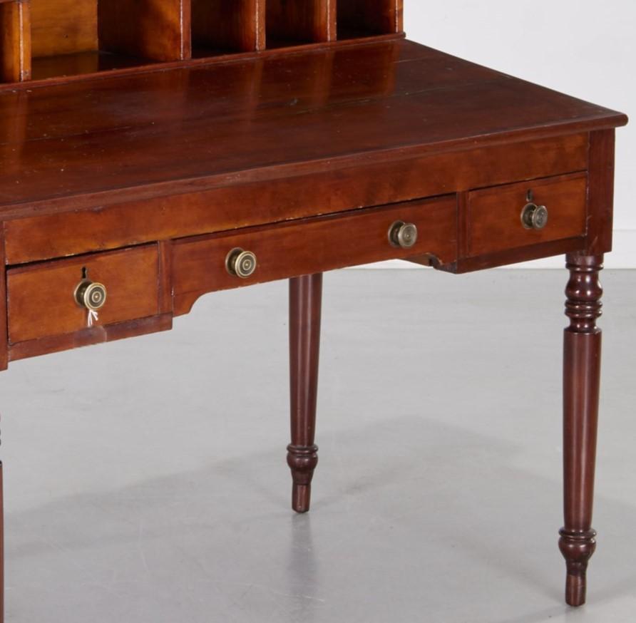 An unusual 19th c., American Sheraton Clerk's Desk. A shaped gallery with a larger rectangular pigeon hole flanked by three square pigeon holes to each side. The slant writing surface is over three drawers, on turned legs. The drawers have lovely
