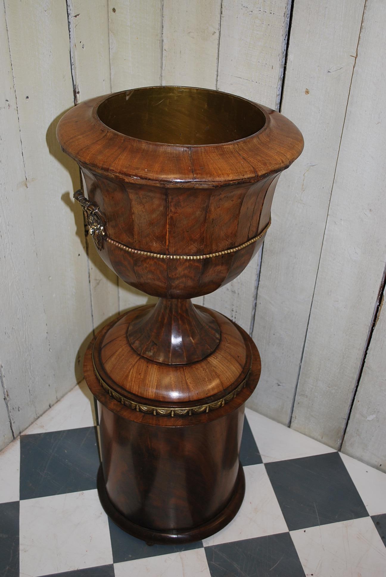 A rare and unusual French jardinière or wine cooler in the form of an urn on a cylindrical pedestal. Made in sections of flamed mahogany, carefully joined together and bolted to the base that opens to reveal a single shelf. Inside the top is a later