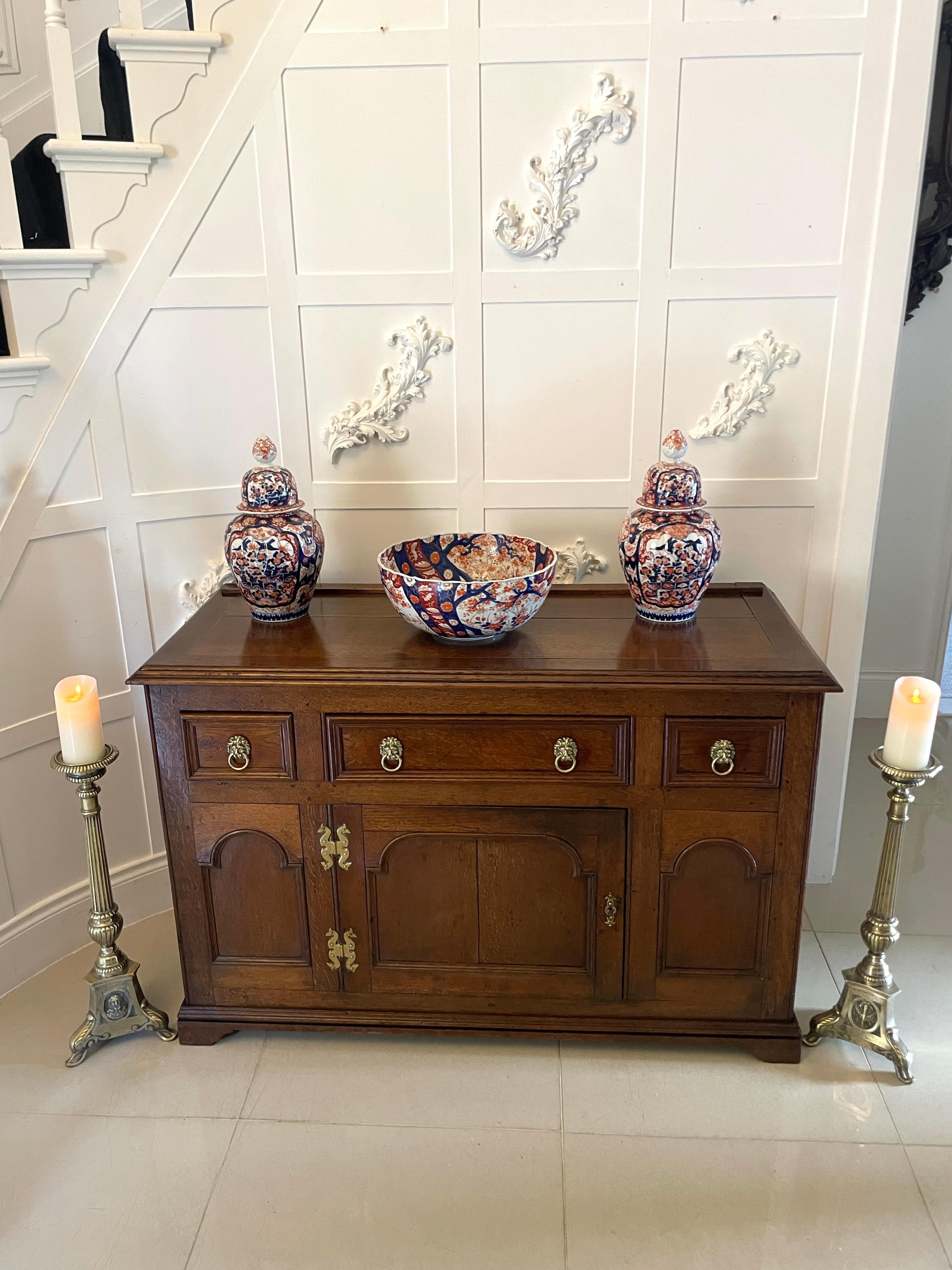 Unusual Antique George III quality oak dresser base having a rectangular shaped quality oak top with stringing inlay above three drawers with attractive lions head brass handles and a moulded edge. 
One large cupboard, moulded panel door to the
