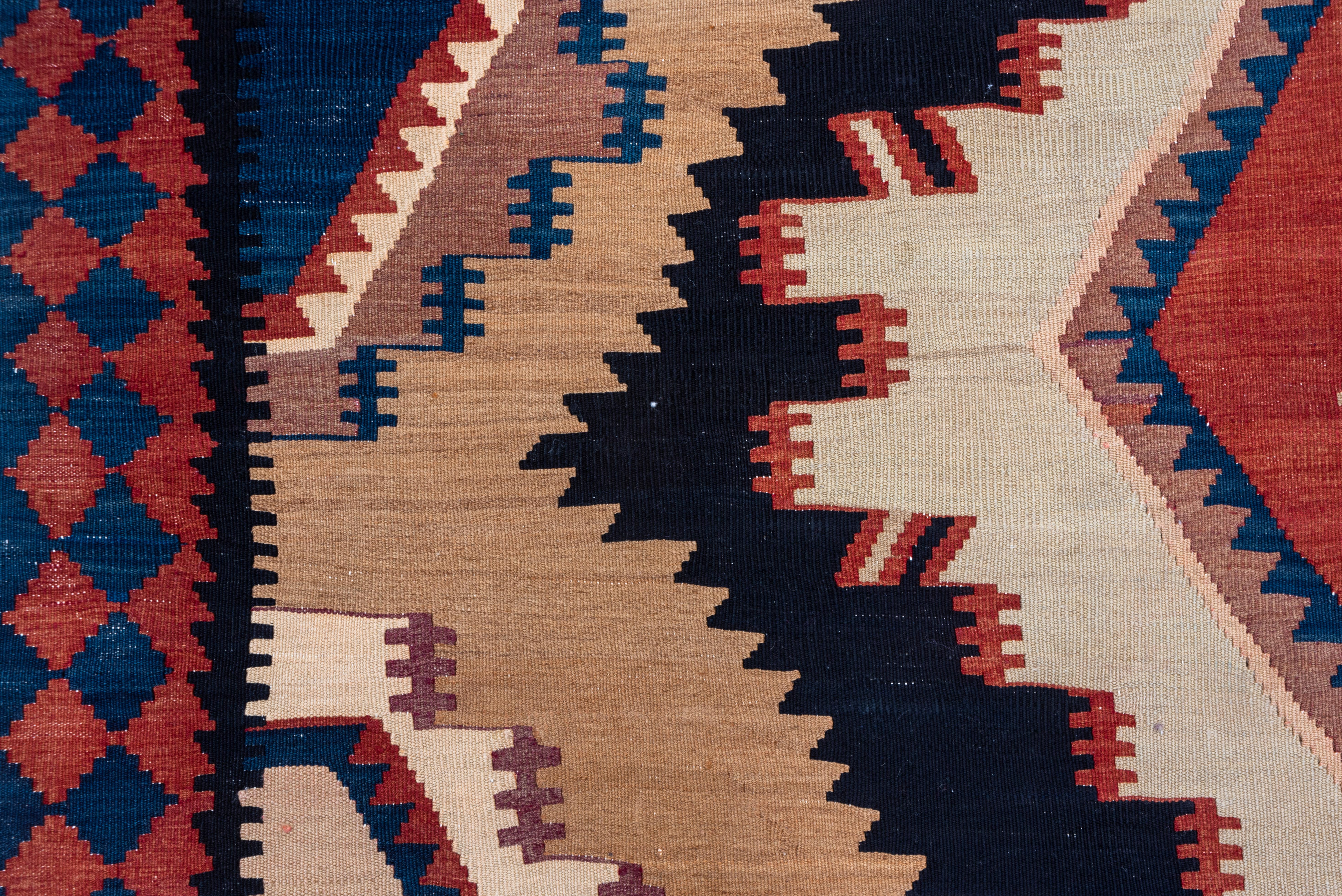 This striking tapestry-weave pileless long carpet shows a deep navy field with a central pole medallion of stepped, layered, conjoint diamonds and lozenges, with half hexagonal filler sat the sides. Red, medium blue, camel, sand and cream accents.