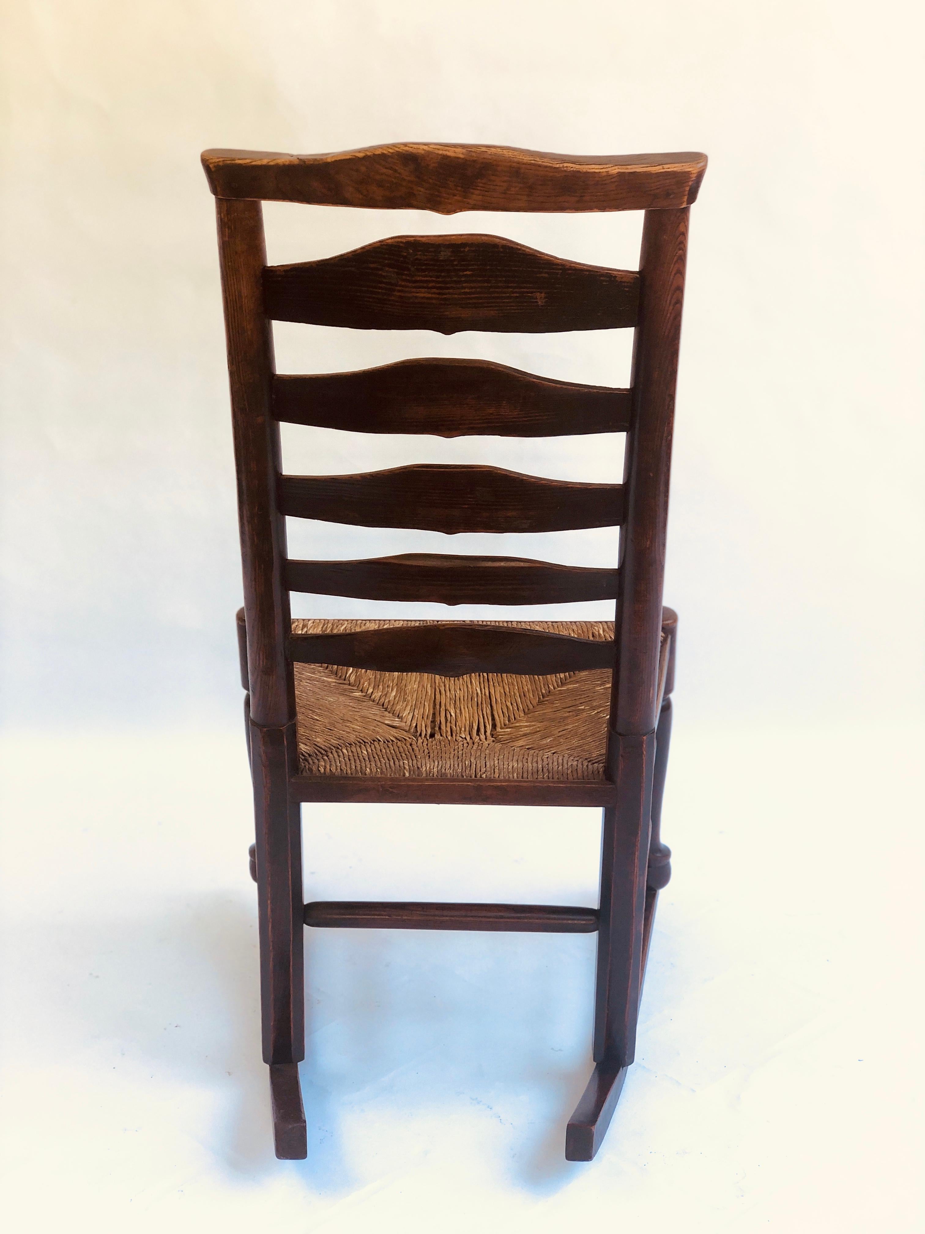 Unusual antique oak ladder back rocking chair having an attractive ladder back with original rush seat. It has shaped pad feet to the front united by turned stretchers and raised on original rockers. This is a lovely item in its original