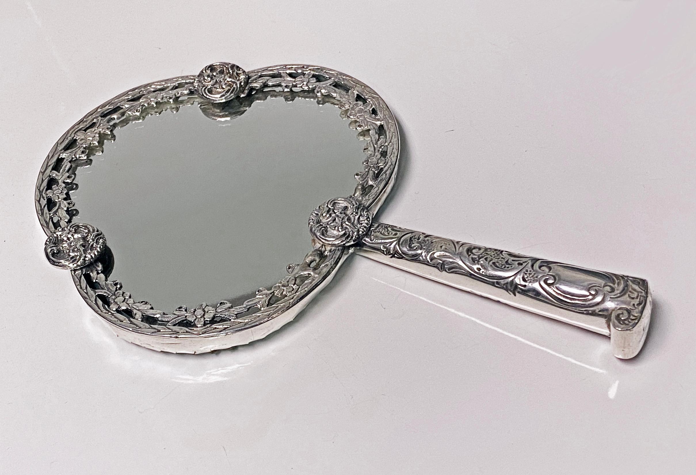 Unusual Antique silver hand mirror, London,1880, Robert Humphries. The front of frame designed with intervals of cherub cupids amidst rosette foliage border, the parasol style handle with foliage decoration. Length: 8.5 inches. Width: 5.1 inches.