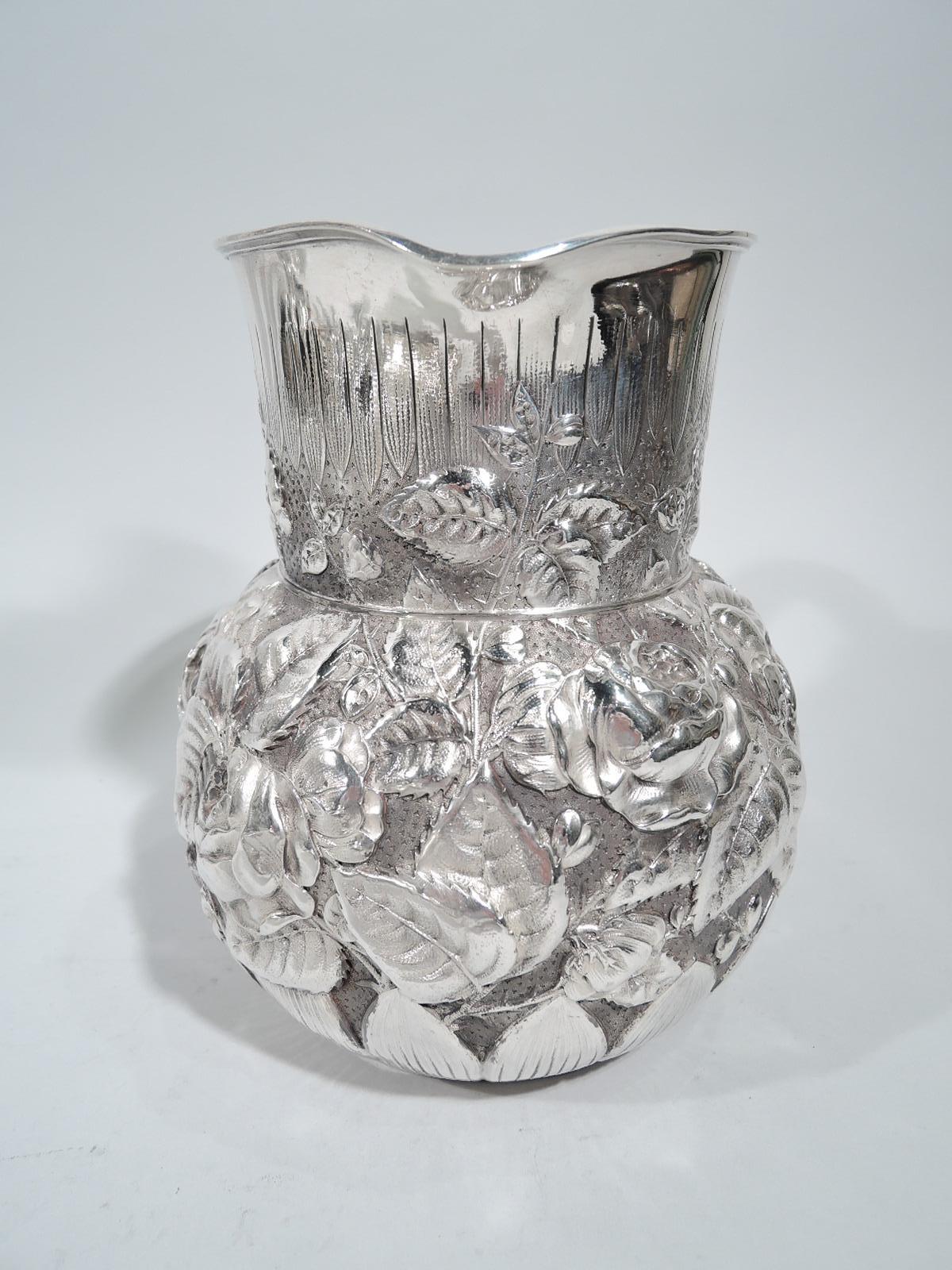 Unusual sterling silver water pitcher. Made by Tiffany & Co. in New York. Globular bowl, straight neck with gently lip spout, and C-scroll handle. Floral repousse in form of pell-mell blooms on stippled ground. Chased vertical leaf border on base.