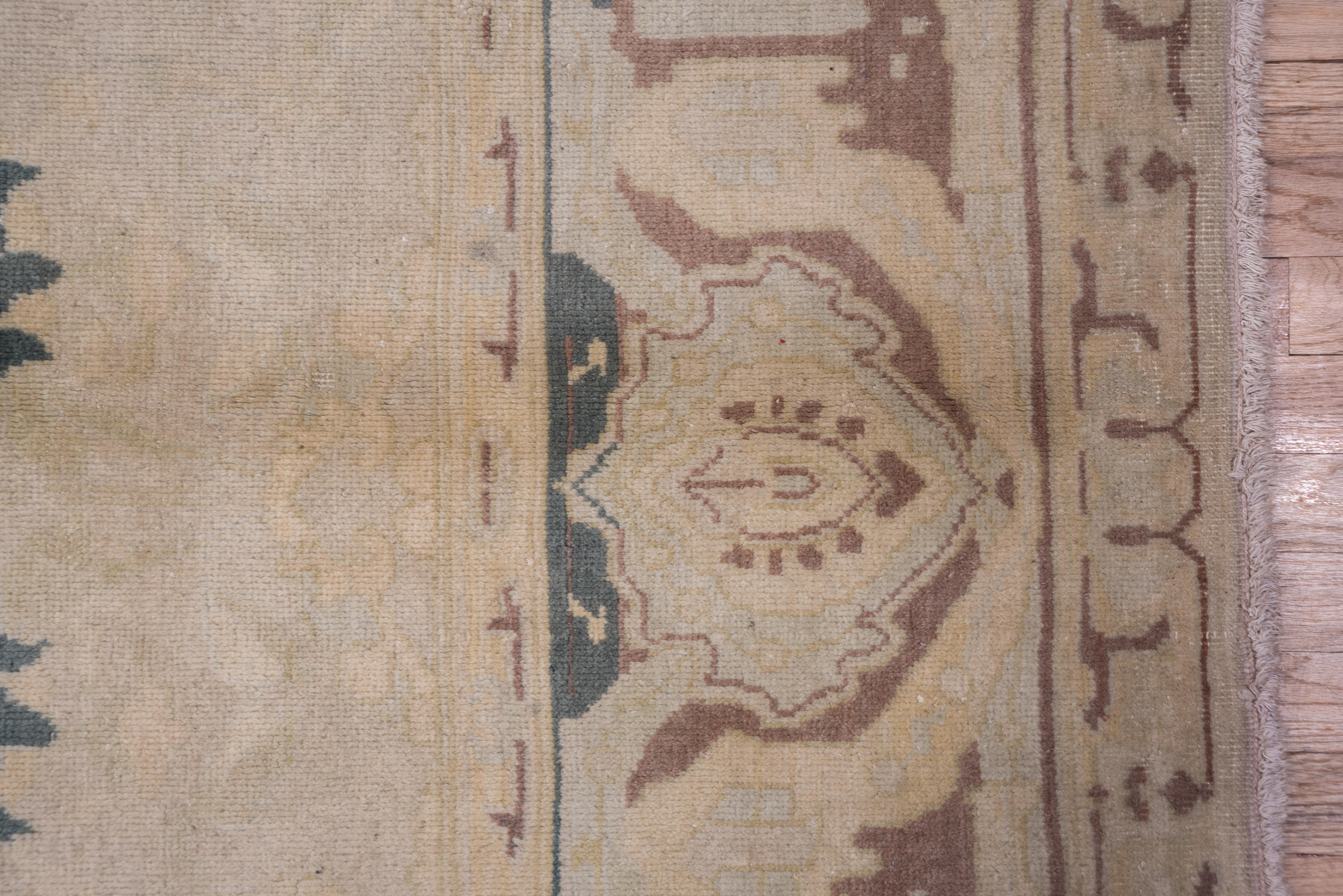 Large brown petal palmettes in erect and lazy positions dominate the central axis of the abrashed beige field, with a stencil pattern mauve border of strapwork and reversing palmettes.