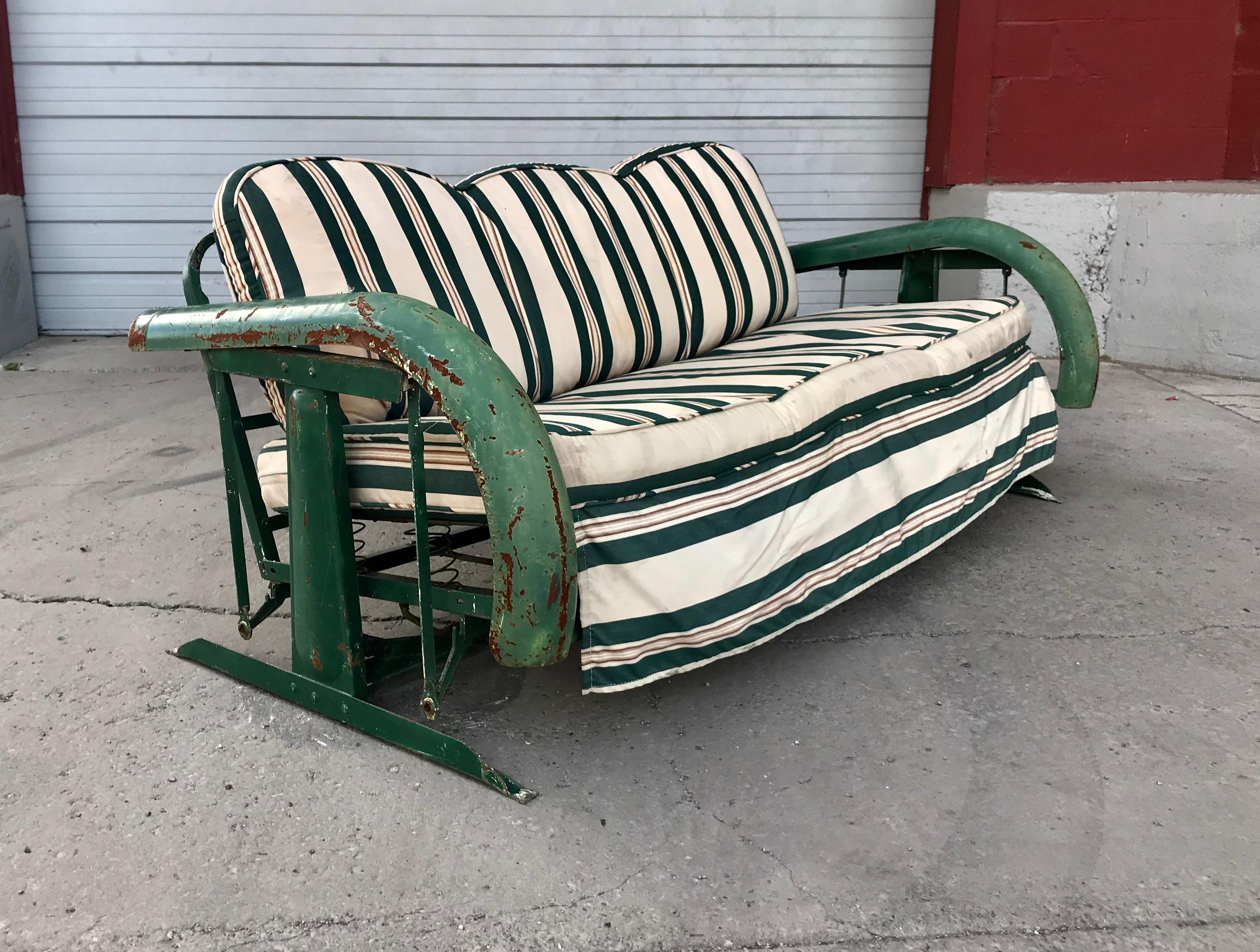 Unusual Art Deco metal porch glider with skirted fenders, circa 1930s. Fabulous design, retains original finish as well as original down filled seat and back striped cushions. Metal fender arms, spring seat. Structurally sound, extremely