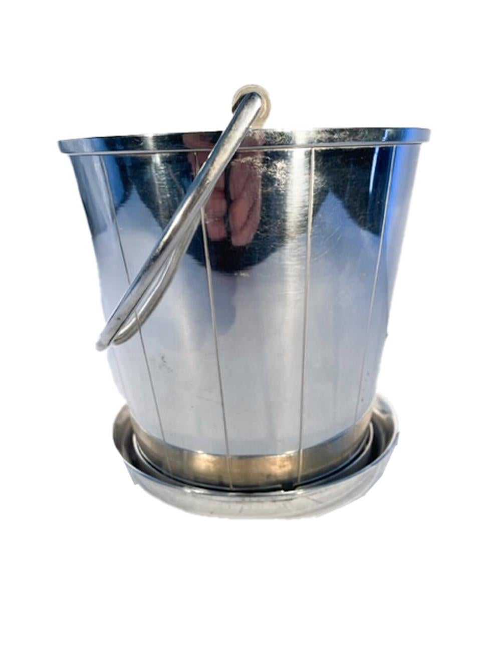 Unusual silver plate ice bucket of pail form with swing handle and incised vertical lines. There is an interior pierced drain plate to hold the ice above water as well as an unusual detachable saucer which is held in place using a twist-lock