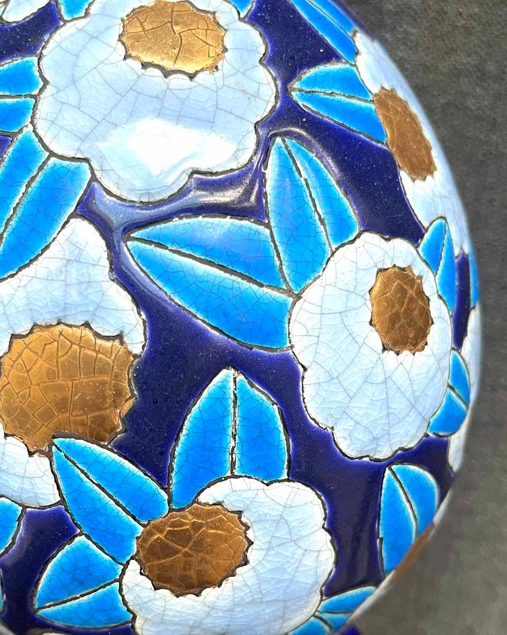 Recouvert de fleurs en pleine floraison et émaillé dans une palette inhabituelle de pervenche, bleu marine, or et bleu ciel, ce vase Art déco de forme ovoïde a été fabriqué par la célèbre entreprise de céramique Longwy en France. Longwy a été créé