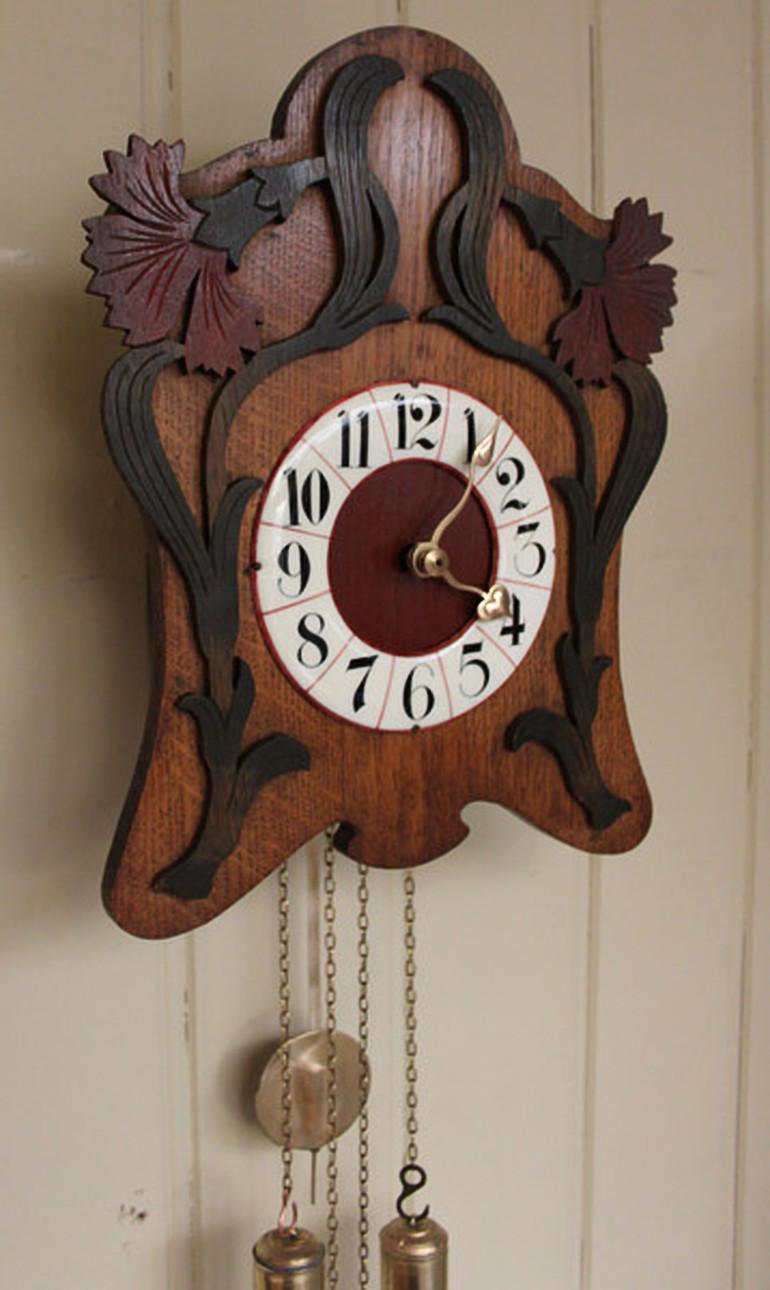 An unusual Art Nouveau wall clock from the Black Forest. It has an oak front with carved, colored applied vine leaves, and an enamel chapter ring with red lines and block numerals. It has a wooden plated movement with bass weights and pendulum that